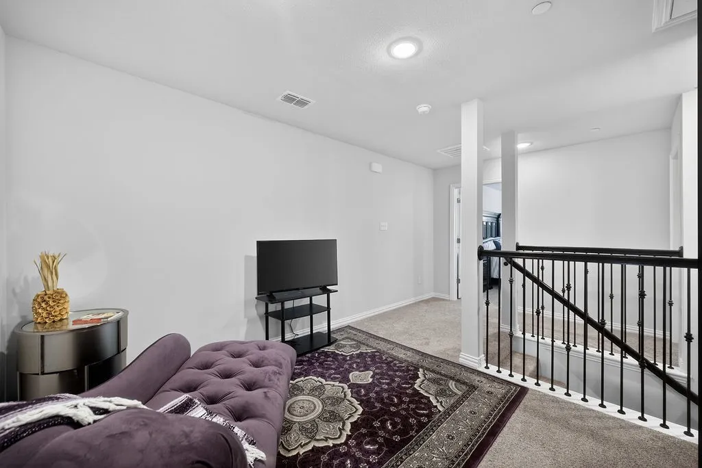 Carpeted second-story landing featuring a wrought iron railing, recessed lighting, and crisp white walls