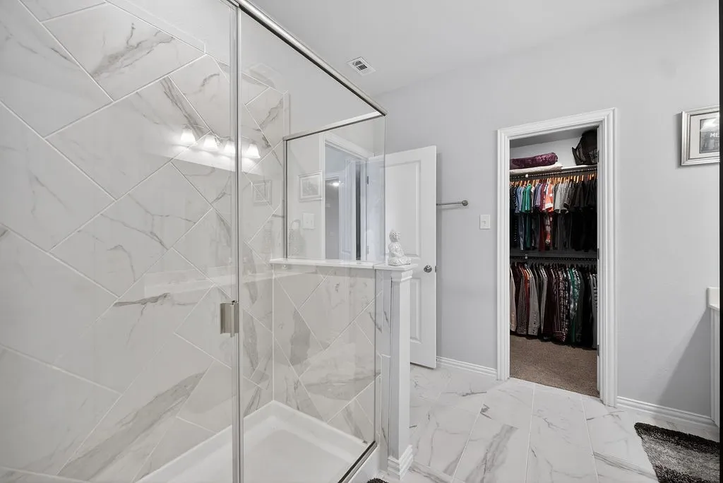 Glass-enclosed shower with full-height marble-look tile surround and a tiled half-wall partition