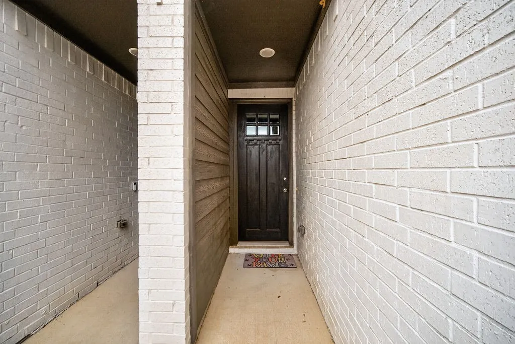 Recessed entryway featuring white brick and horizontal siding, a dark wood-finish door with glass panels, and a concrete pathway