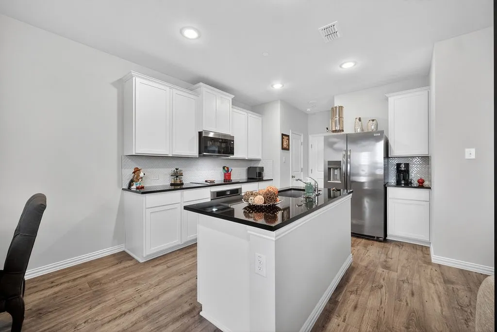 Kitchen featuring wood-finish flooring, white cabinetry, black countertops, and stainless steel appliances
