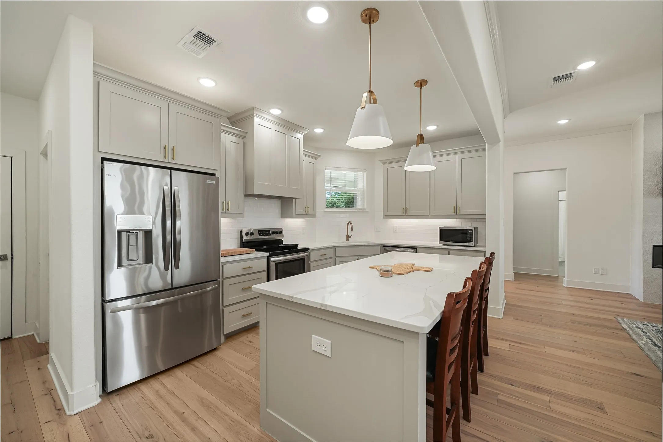 Modern kitchen featuring an expansive center island with seating, light wood-finish flooring, recessed lighting, stainless steel appliances, and light-toned cabinetry