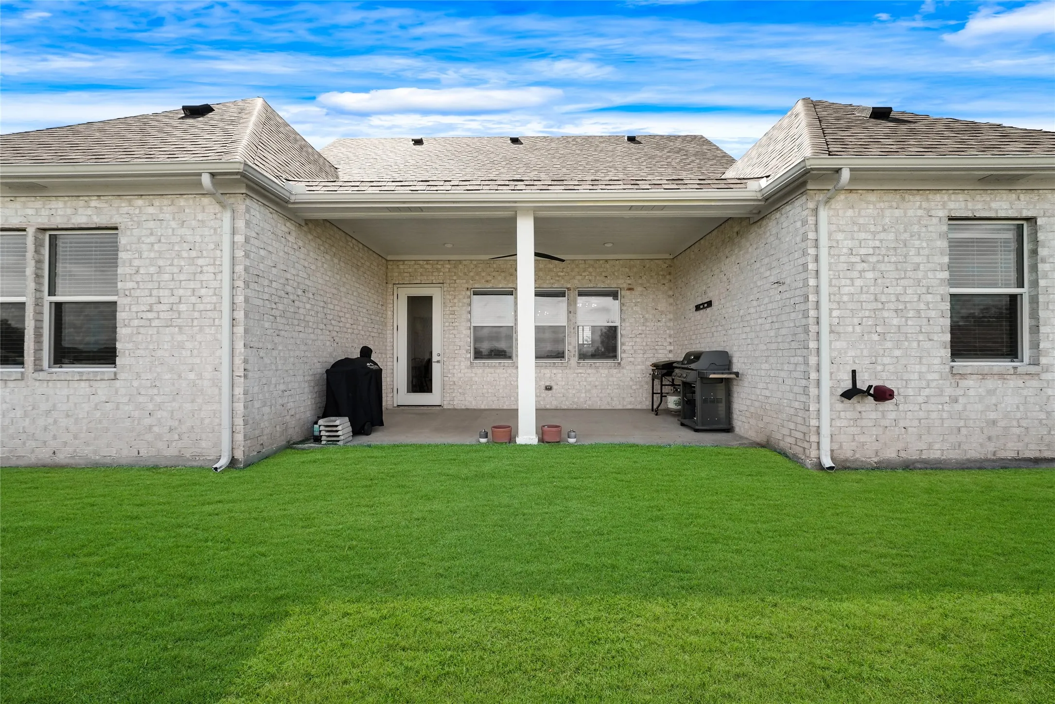 Rear exterior featuring light-colored brick siding, a covered patio, and a spacious lawn