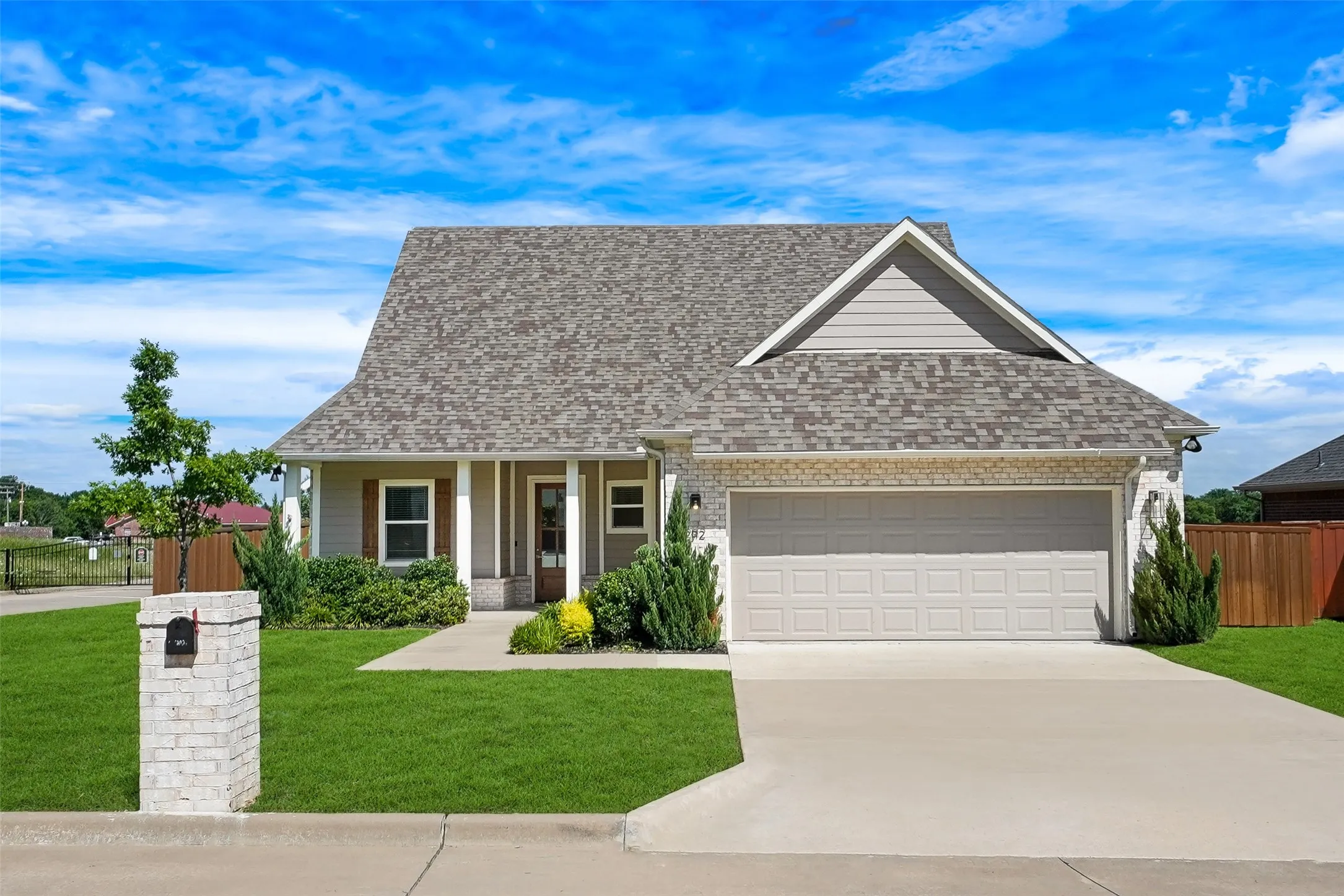 Single-story residence featuring a two-car garage, brick and siding exterior, front porch with columns, a concrete driveway, and a manicured lawn