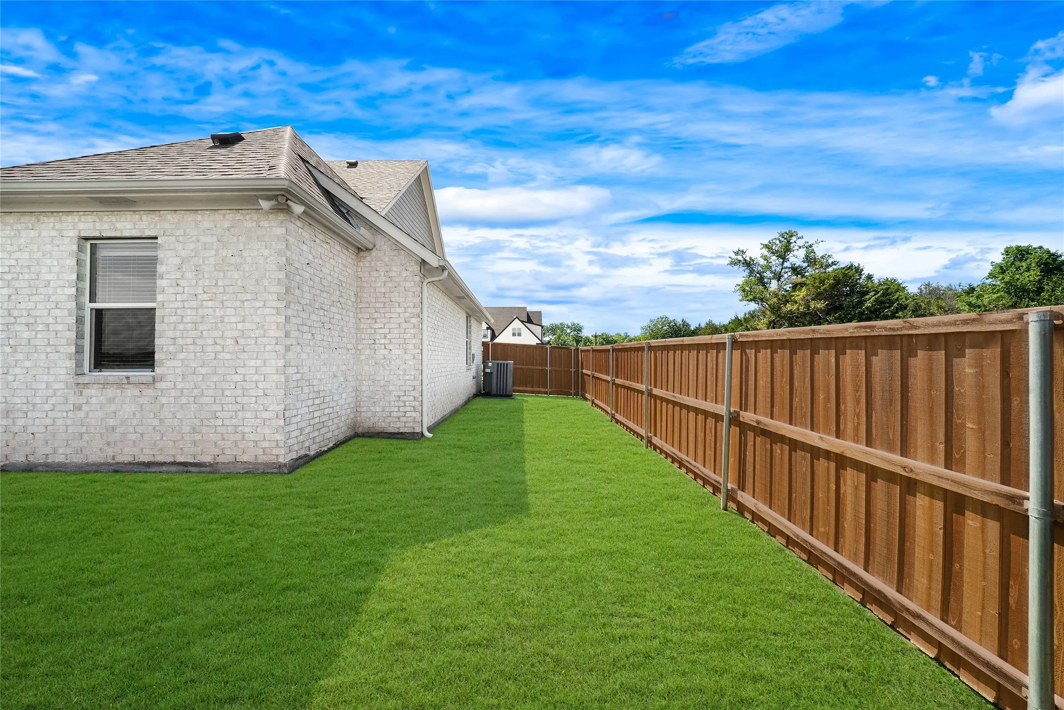 Expansive side yard featuring a manicured lawn, a stained wood privacy fence, and white brick exterior