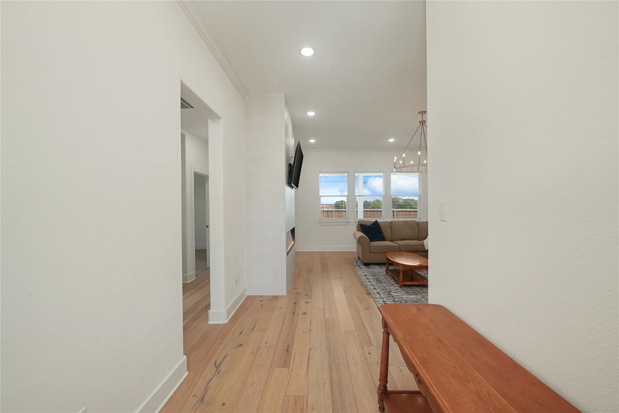 Open-concept living space featuring light wood-finish flooring, recessed lighting, and a modern chandelier