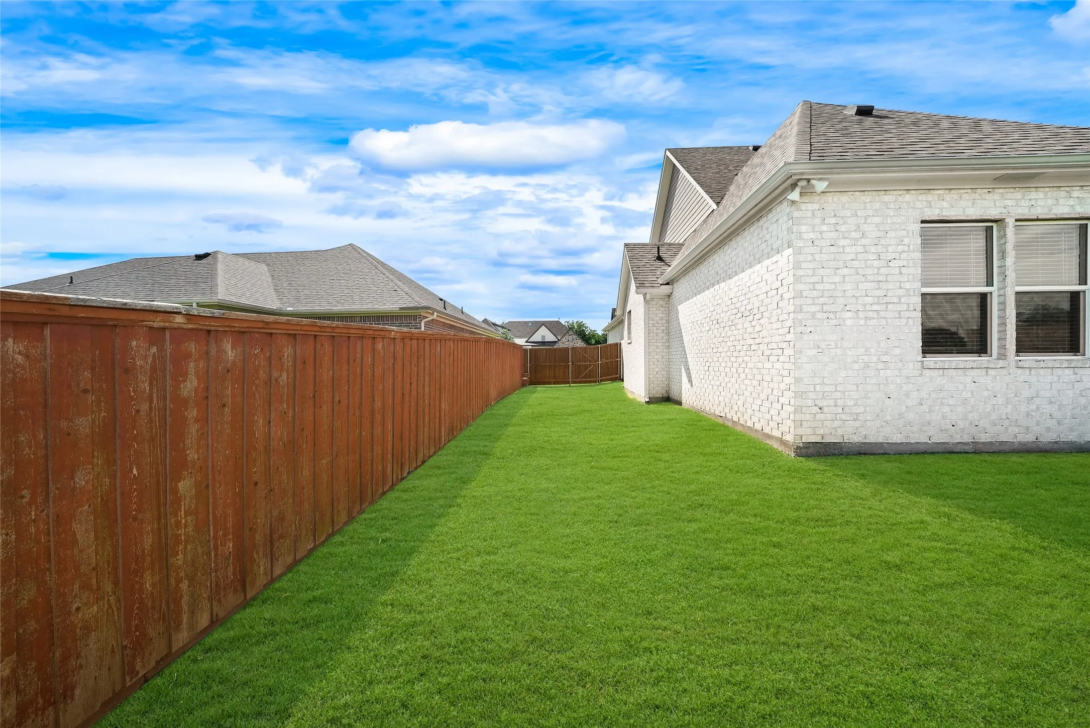 Expansive side yard featuring a manicured lawn, a stained wood privacy fence, and white brick exterior