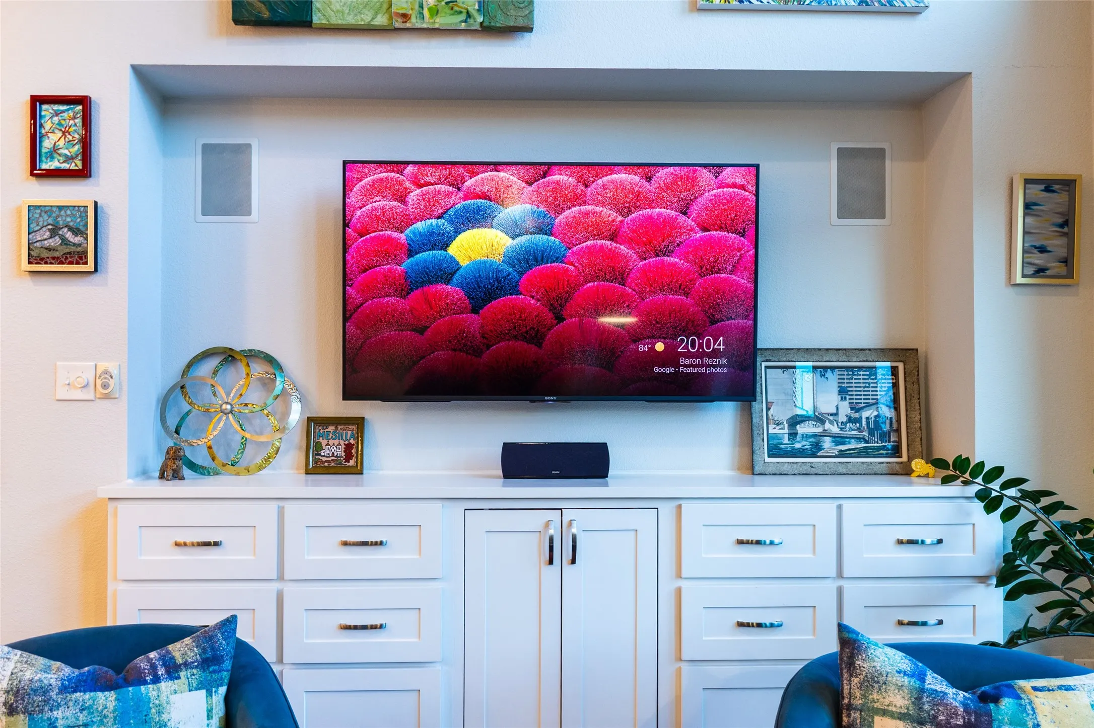 Built-in media center featuring a recessed television, integrated speakers, white cabinetry with silver-tone hardware, and a solid surface countertop