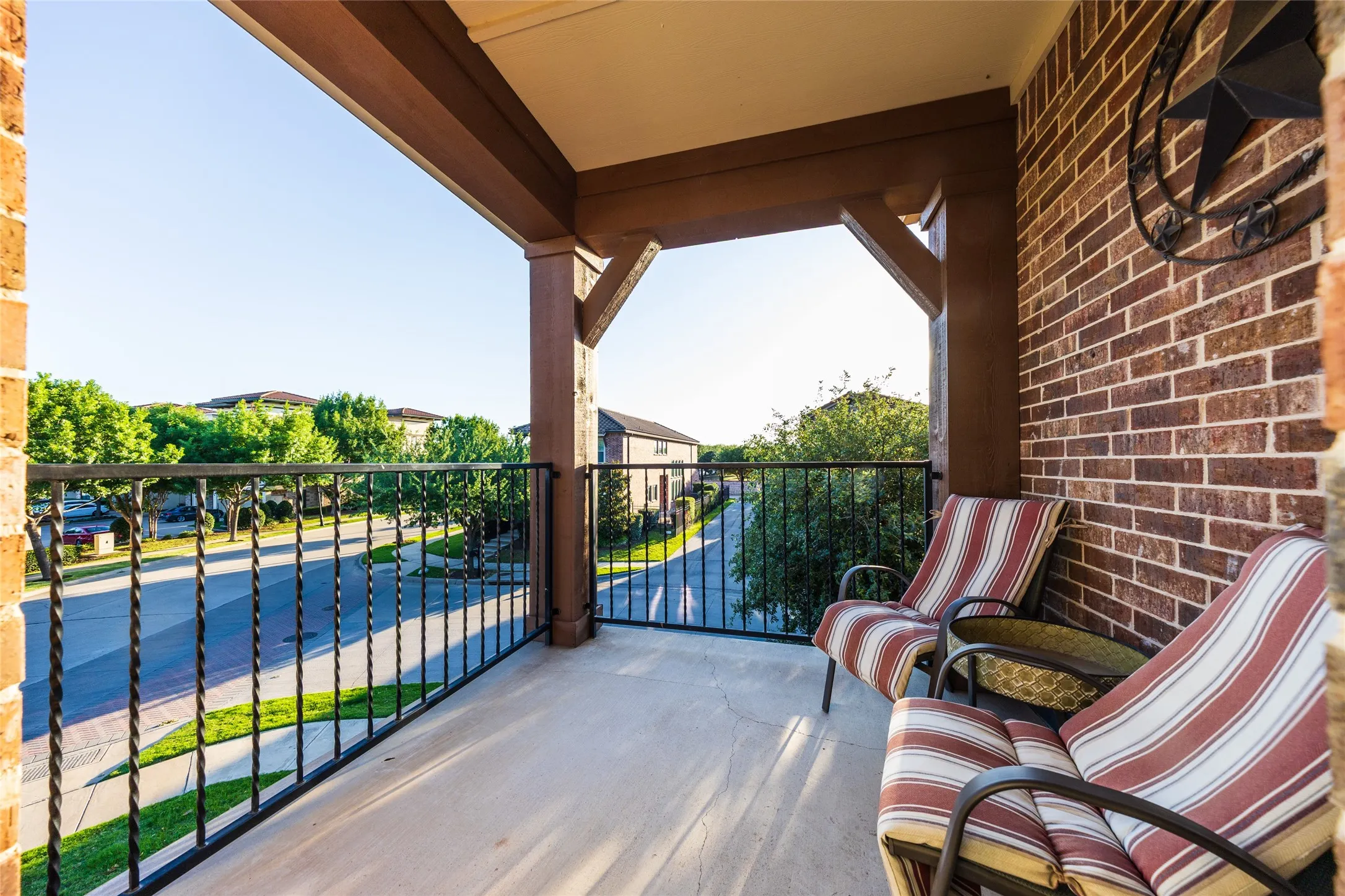 Covered balcony off Primary Suite featuring a concrete floor, brick wall, and wrought iron railing
