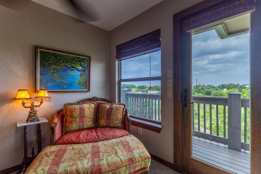 This sitting area in the primary suite is situated at a 2nd exit leading to the full wrap-around balcony; views from this side include the lake to the right and the guest house, playground and acreage to the left.