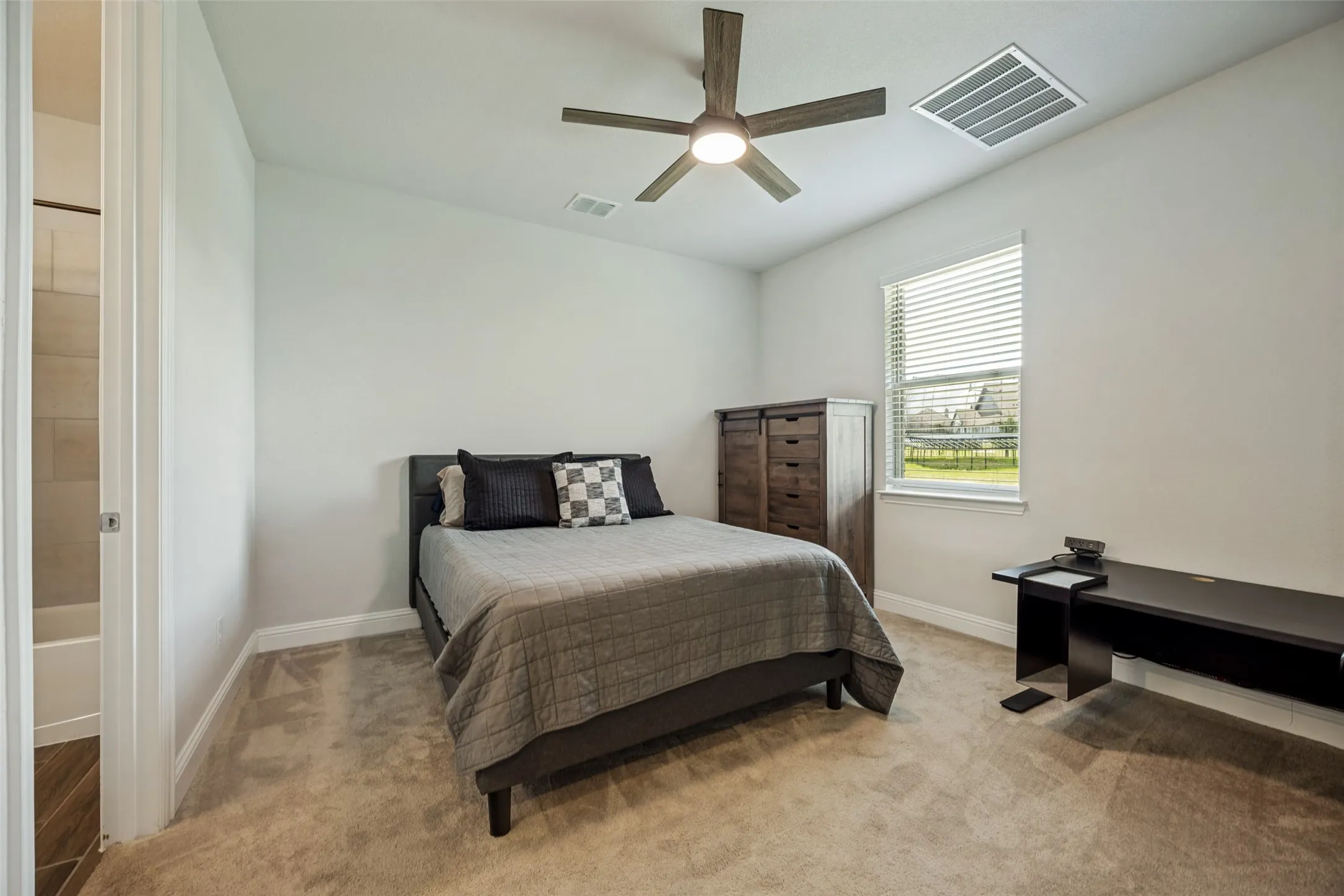 Light-filled multi-generational bedroom featuring plush carpeting, a ceiling fan with integrated lighting, a window with blinds, and white baseboards