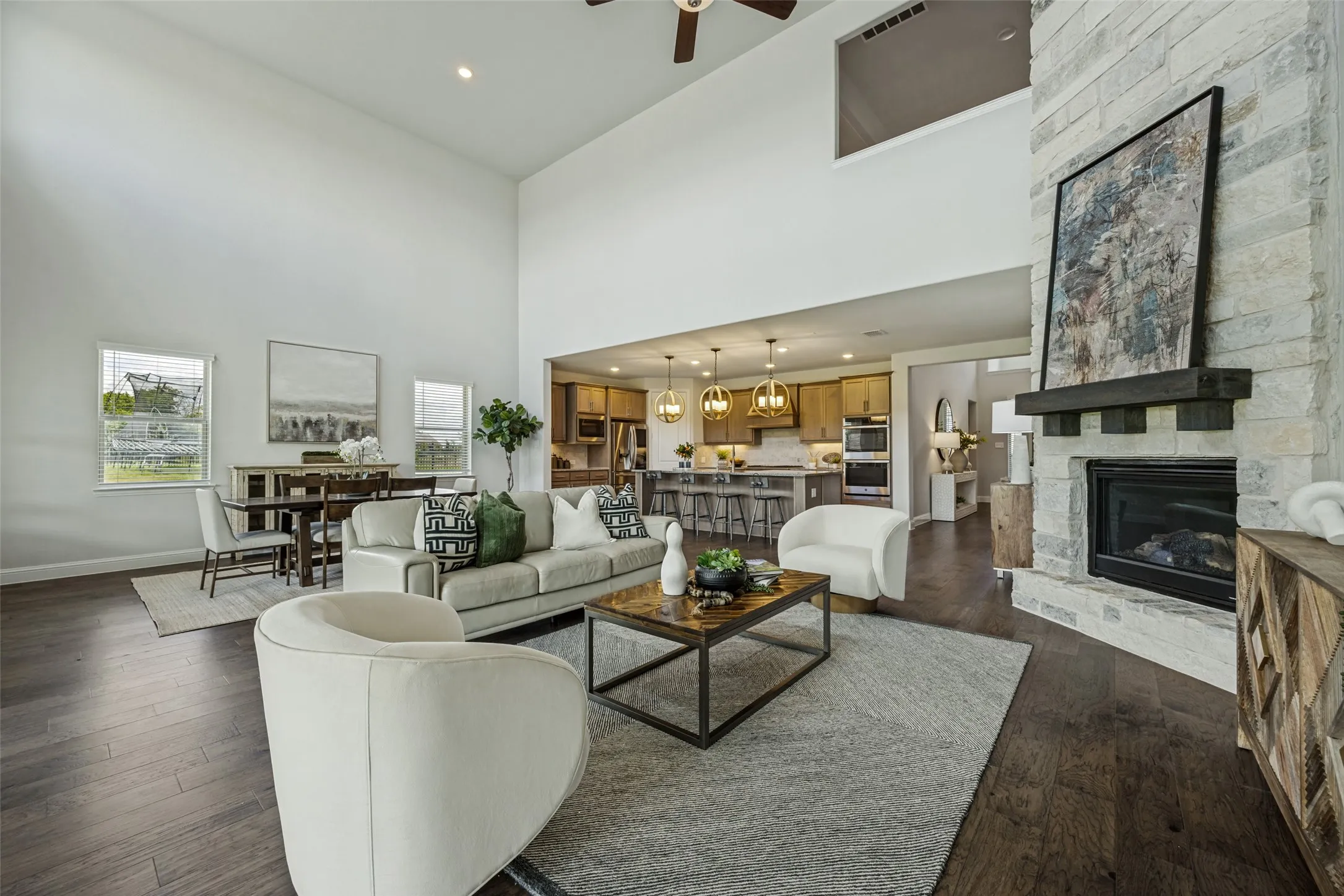 Open-concept living space featuring high ceilings, wood-finish flooring, and a stone fireplace with a dark wood mantel