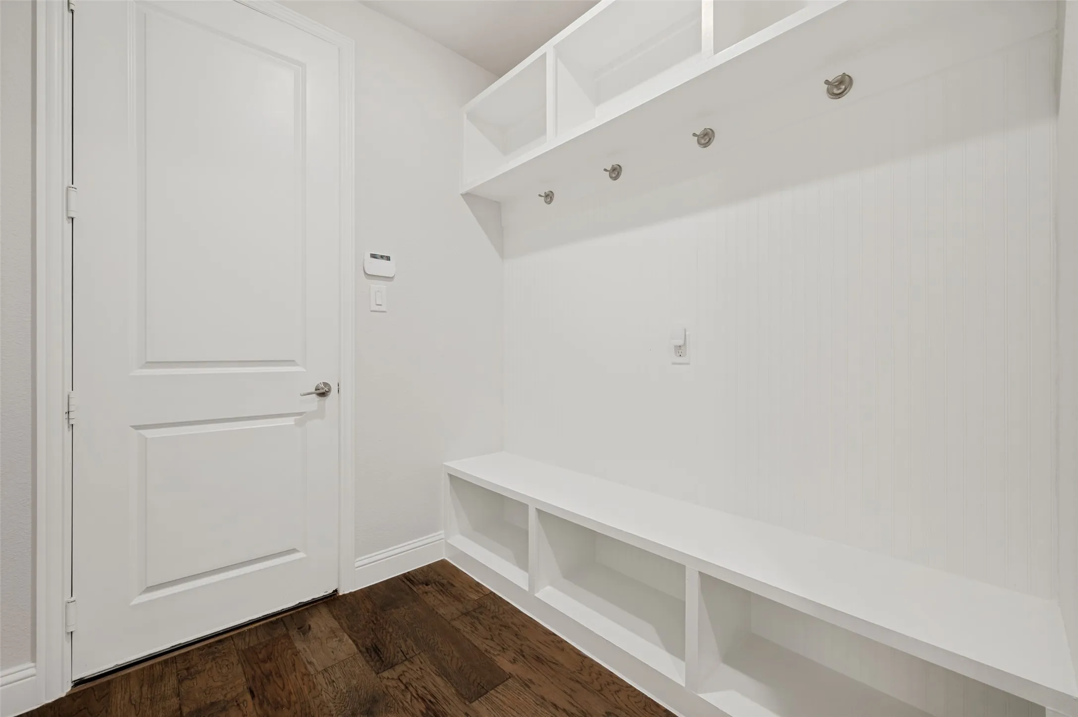 Entryway mudroom featuring built-in white cabinetry, open shelving, integrated bench seating, and wood-finish flooring