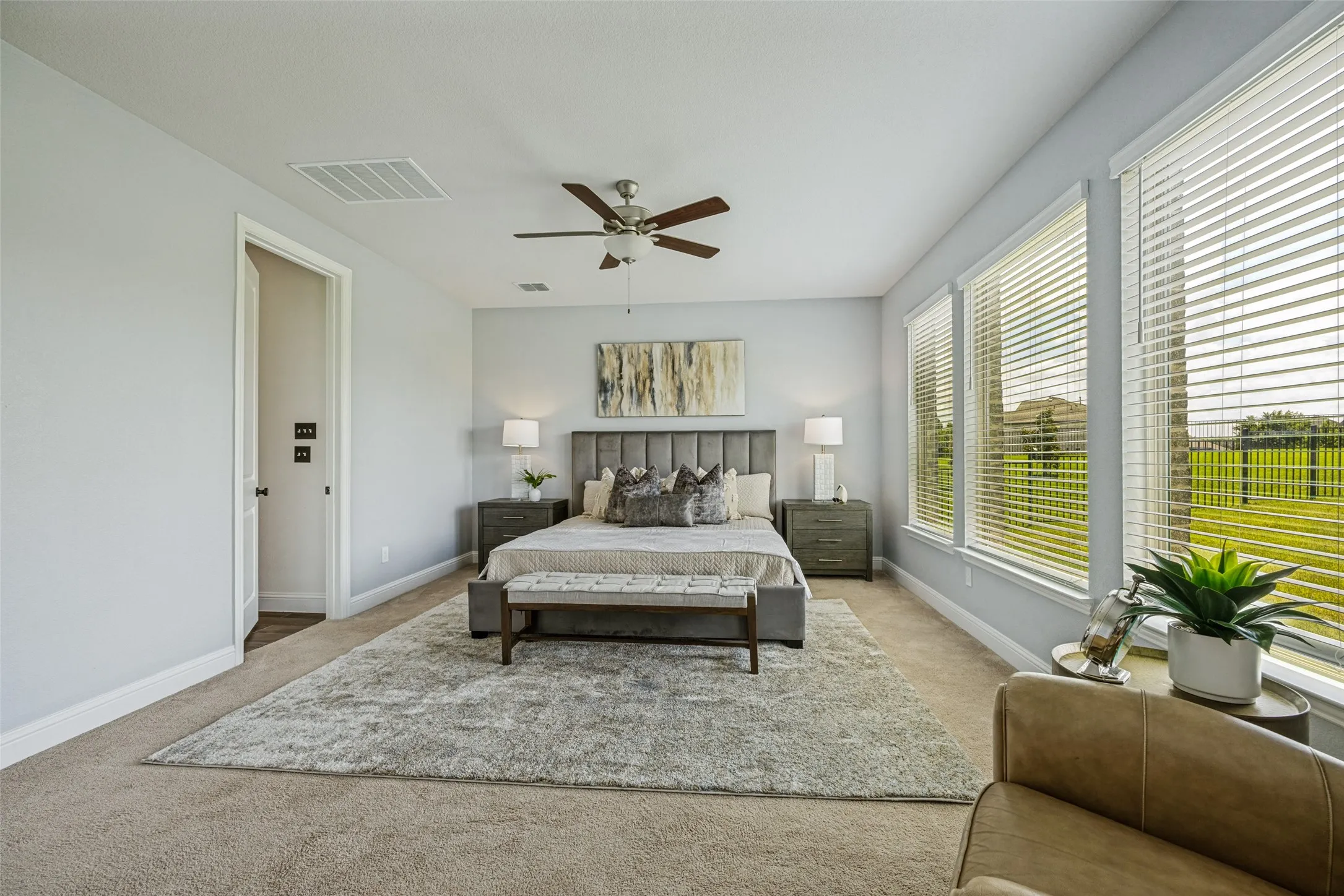 Spacious room featuring multiple windows with blinds, a ceiling fan, light gray wall paint, and carpeting