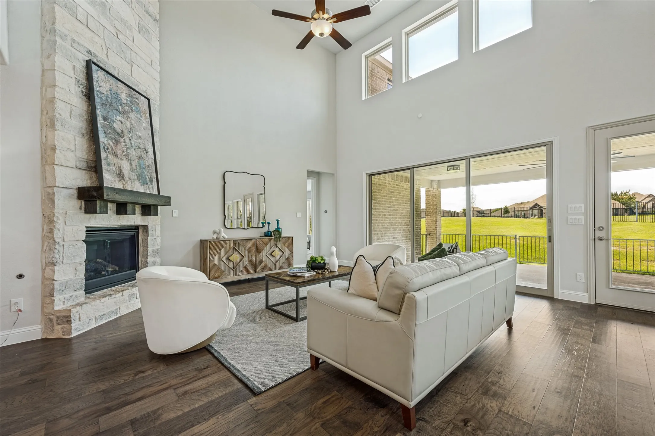 Two-story living area featuring a stone fireplace with a dark wood mantel, high ceilings, wood-finish flooring, and a ceiling fan