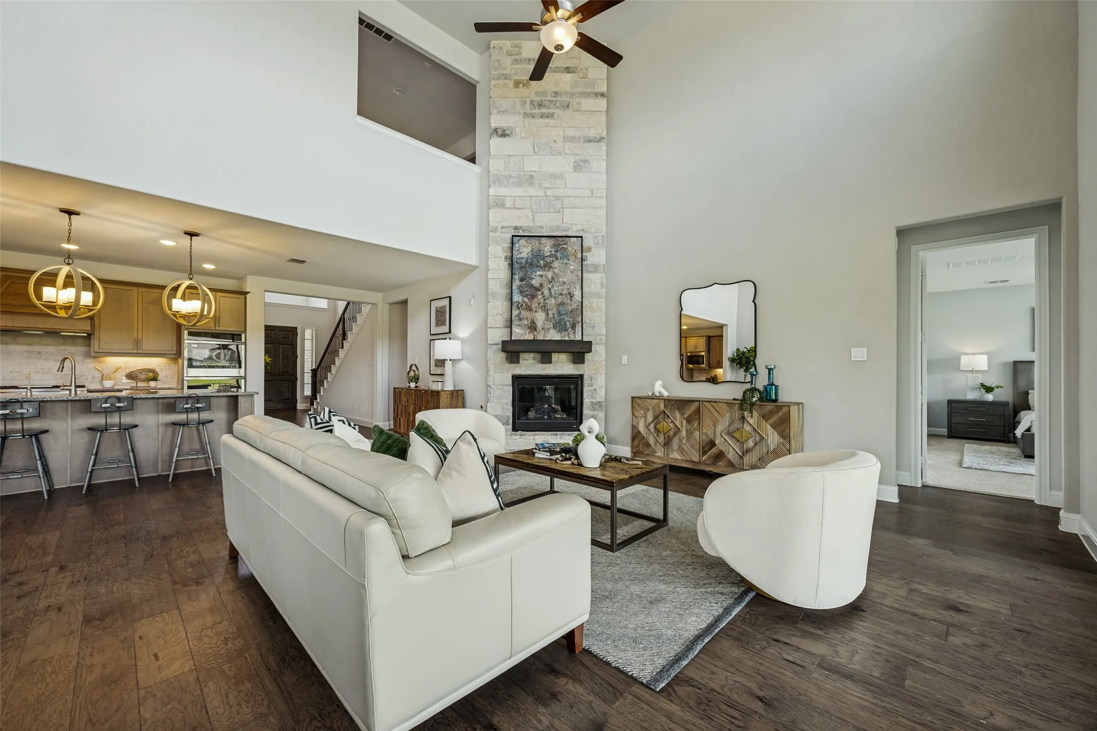 Spacious living area featuring a vaulted ceiling with a ceiling fan, a floor-to-ceiling stone-clad fireplace with a mantel, and dark wood-finish flooring