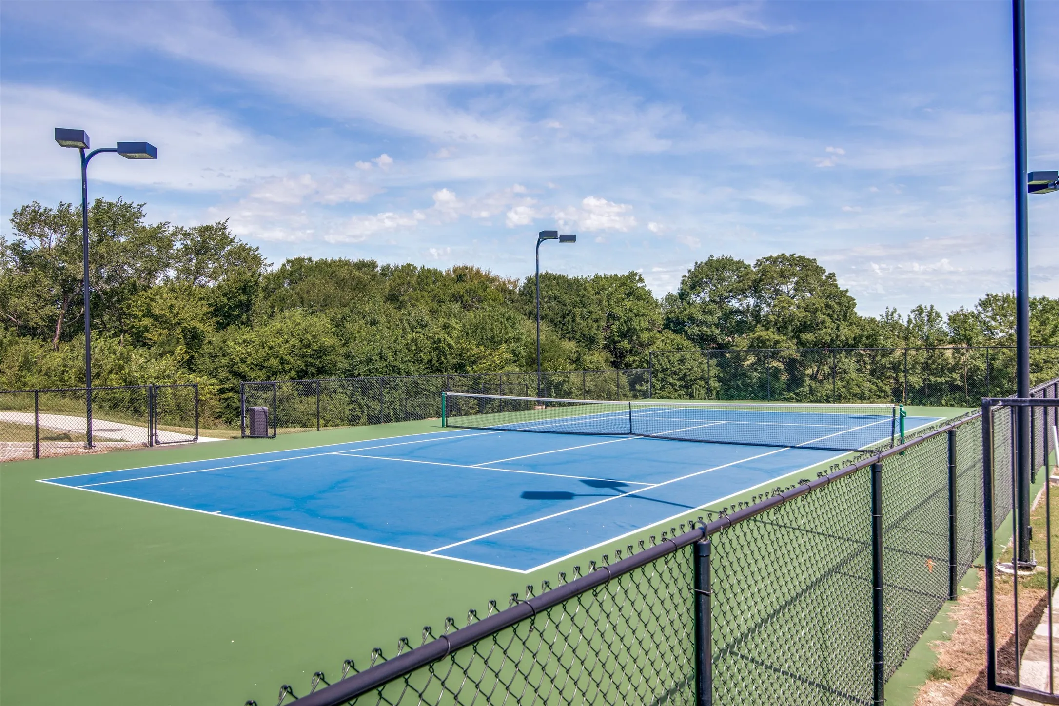 Outdoor tennis court with a blue playing surface and green surrounds