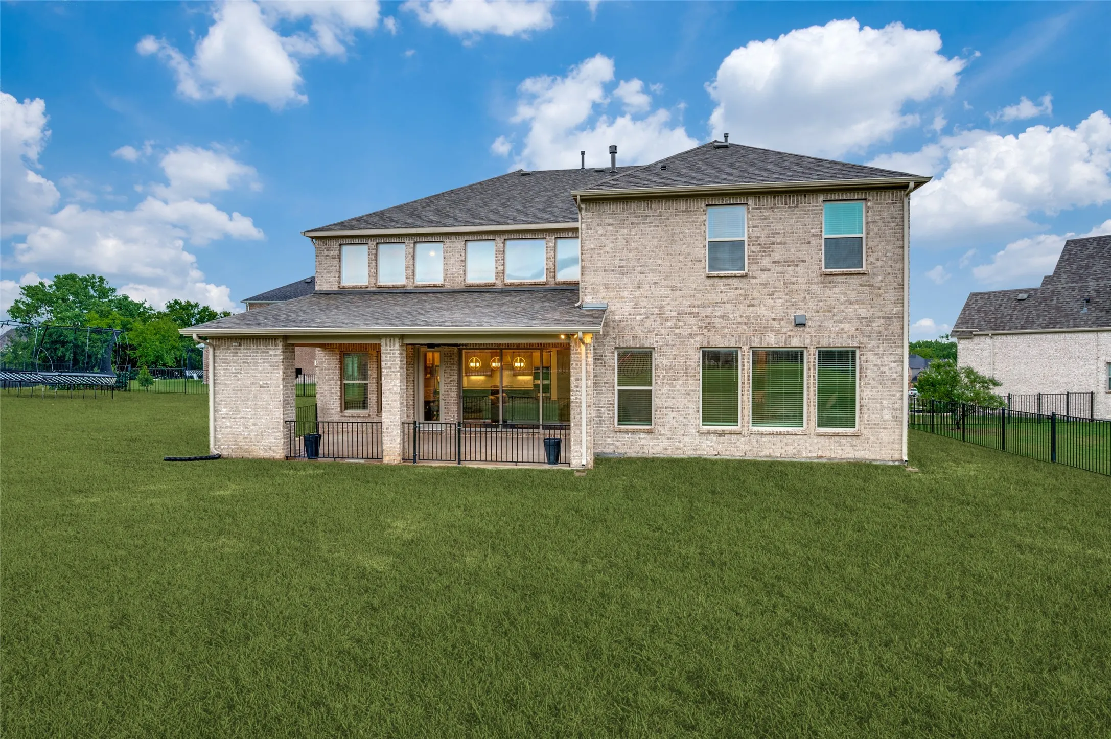Expansive green lawn bordering a two-story brick exterior with a covered patio featuring a black railing