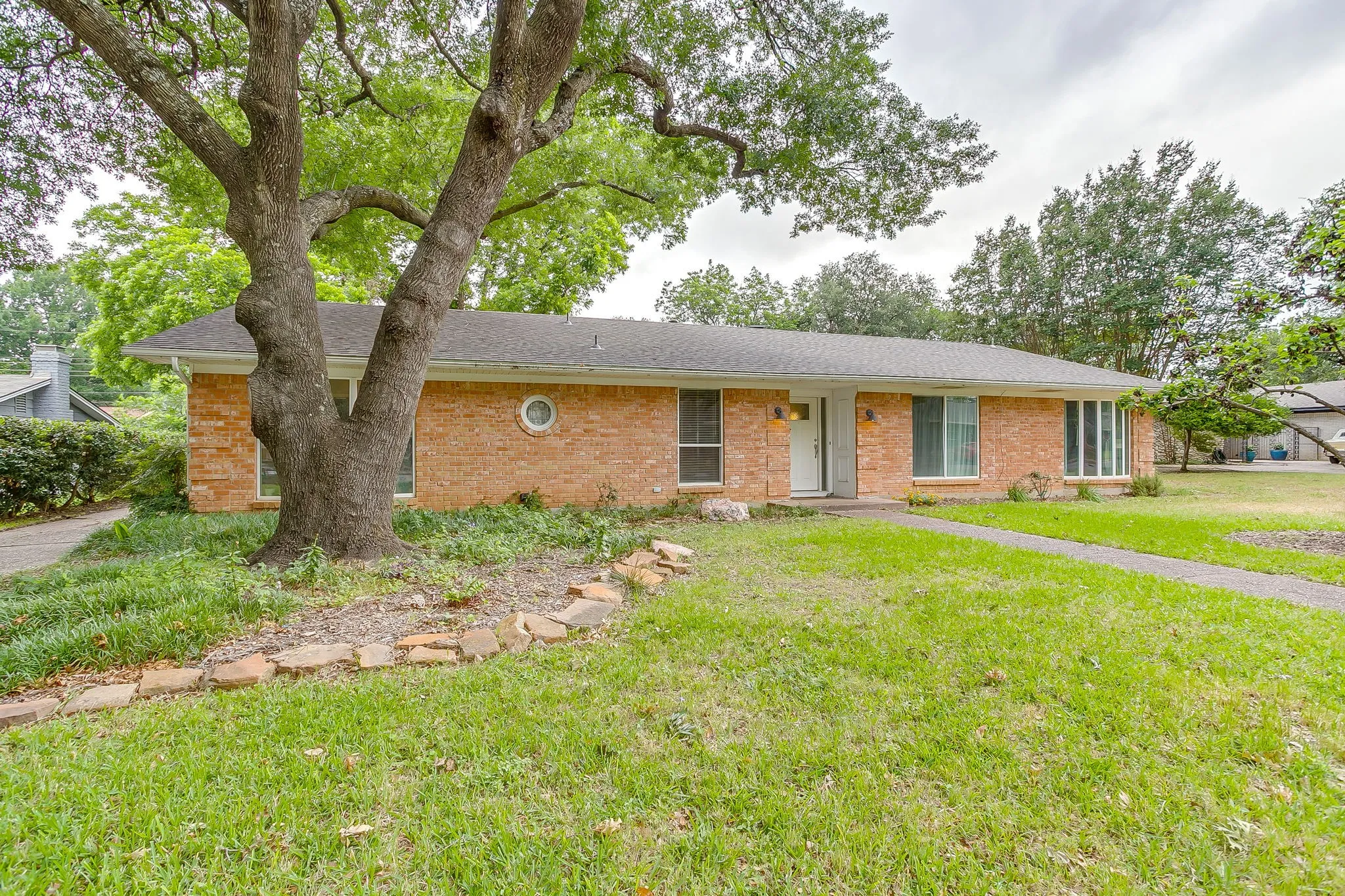 Brick exterior residence featuring a mature tree, front lawn, and a sidewalk leading to the front entry