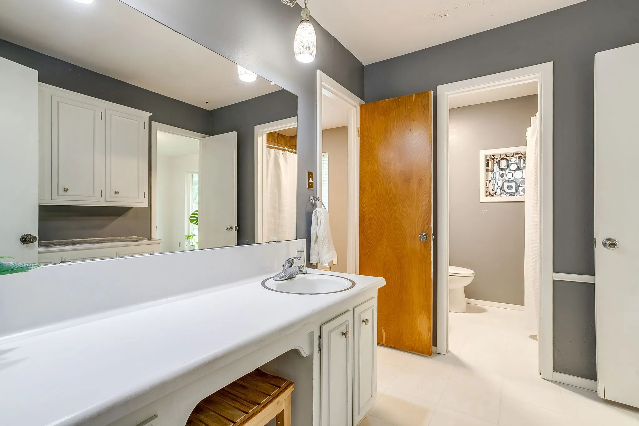 Bathroom vanity featuring a white countertop with an integrated sink, white cabinetry with silver hardware, and an expansive wall-mounted mirror
