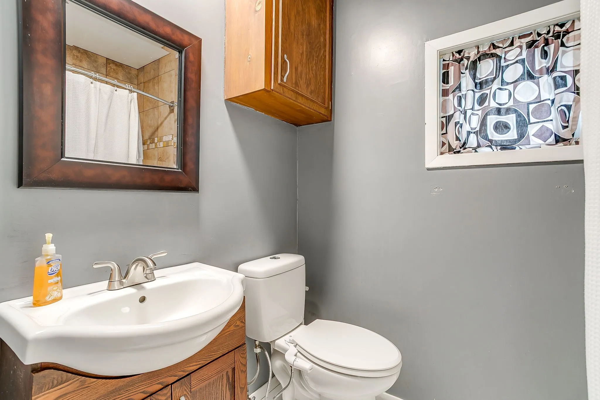 Bathroom featuring a white pedestal sink with a chrome faucet, a framed mirror, and a wood-finish vanity cabinet