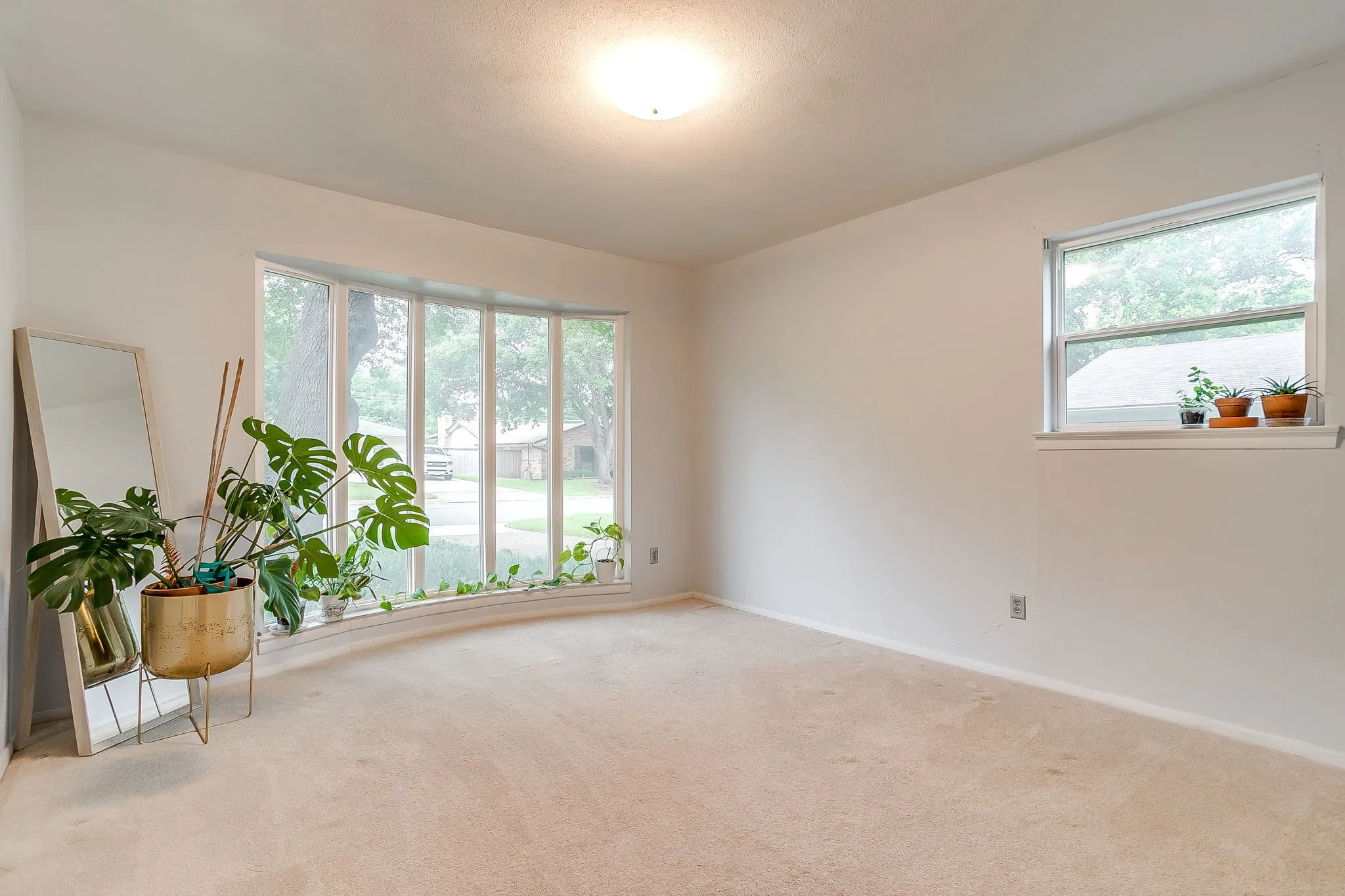 Bright room featuring a large bay window, neutral carpeting, light-toned walls, and a ceiling-mounted light fixture
