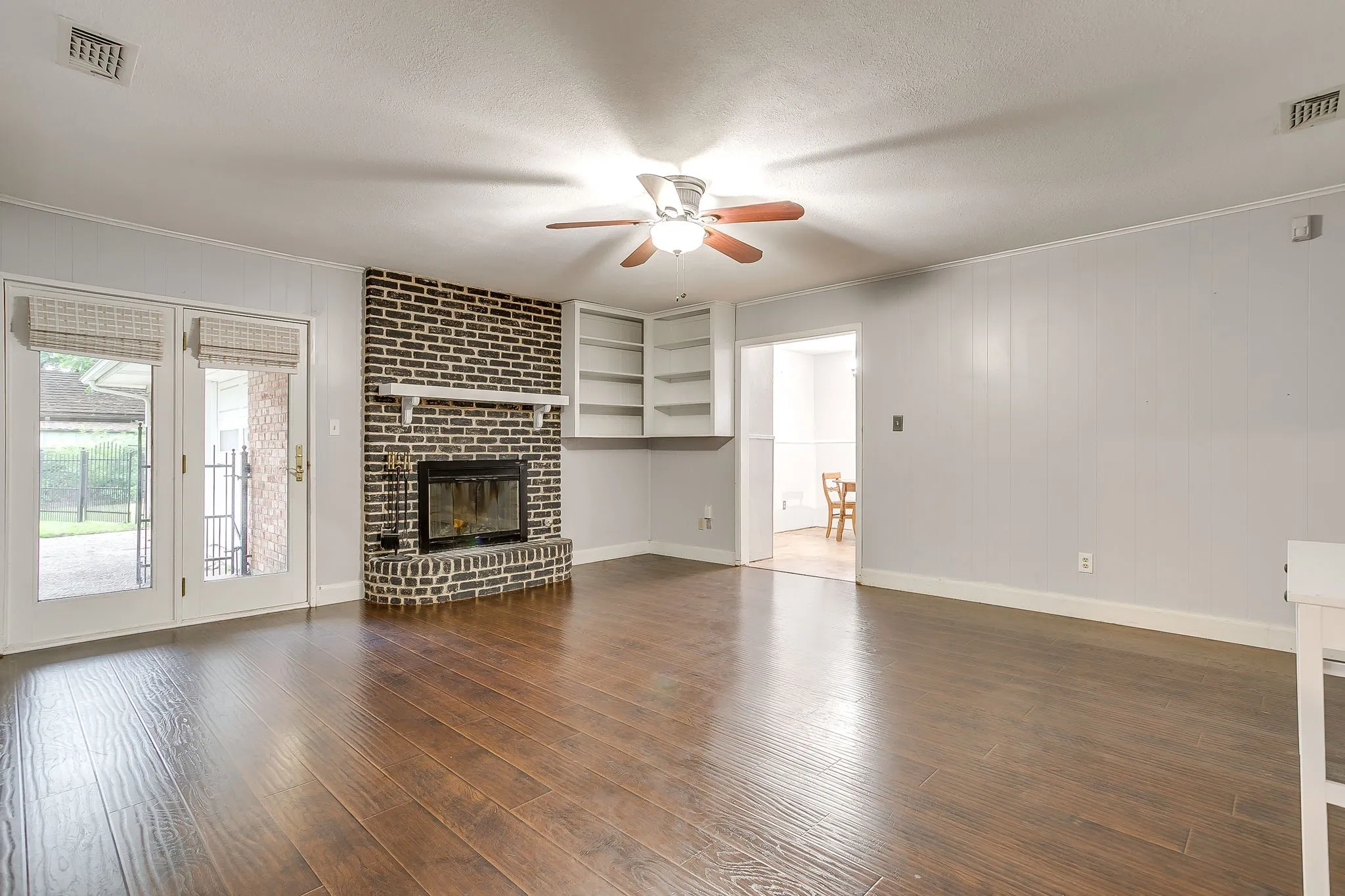 Spacious living area featuring wood-finish flooring, a brick fireplace with a white mantel, and built-in shelving