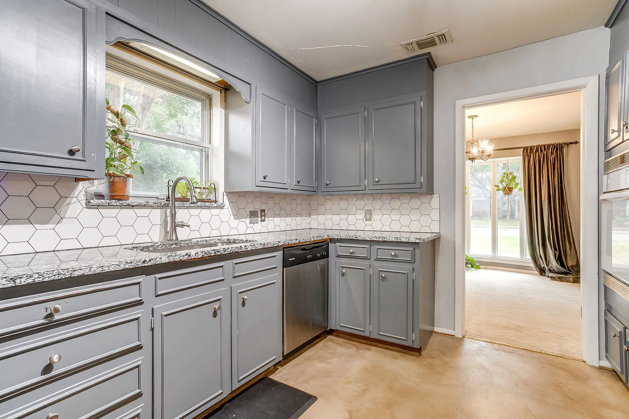 Kitchen featuring grey cabinetry, white hexagonal tile backsplash, stainless steel sink with a gooseneck faucet, and mottled grey countertops
