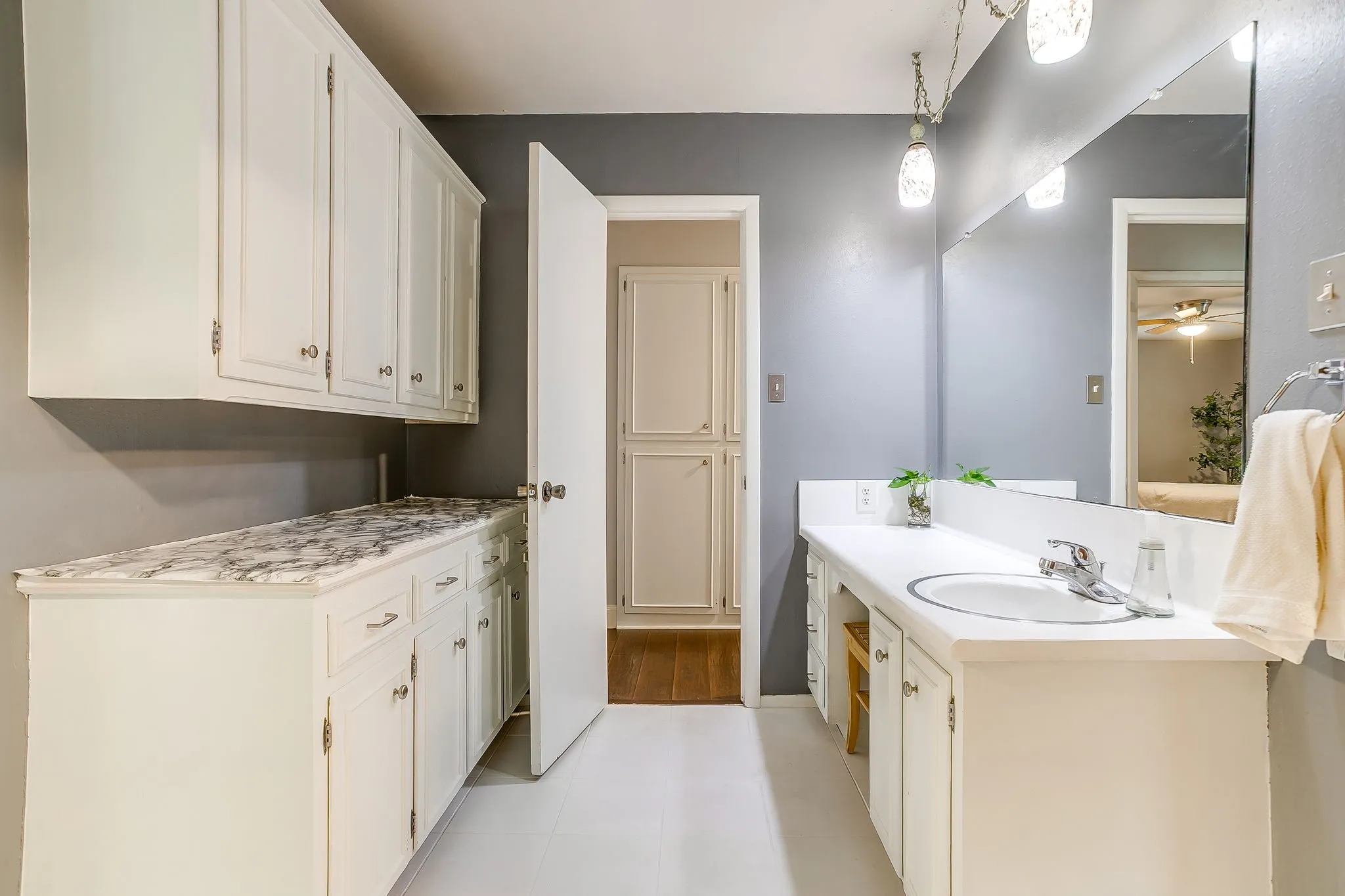 Bathroom featuring a single vanity with an integrated sink, an expansive mirror, and overhead pendant lighting