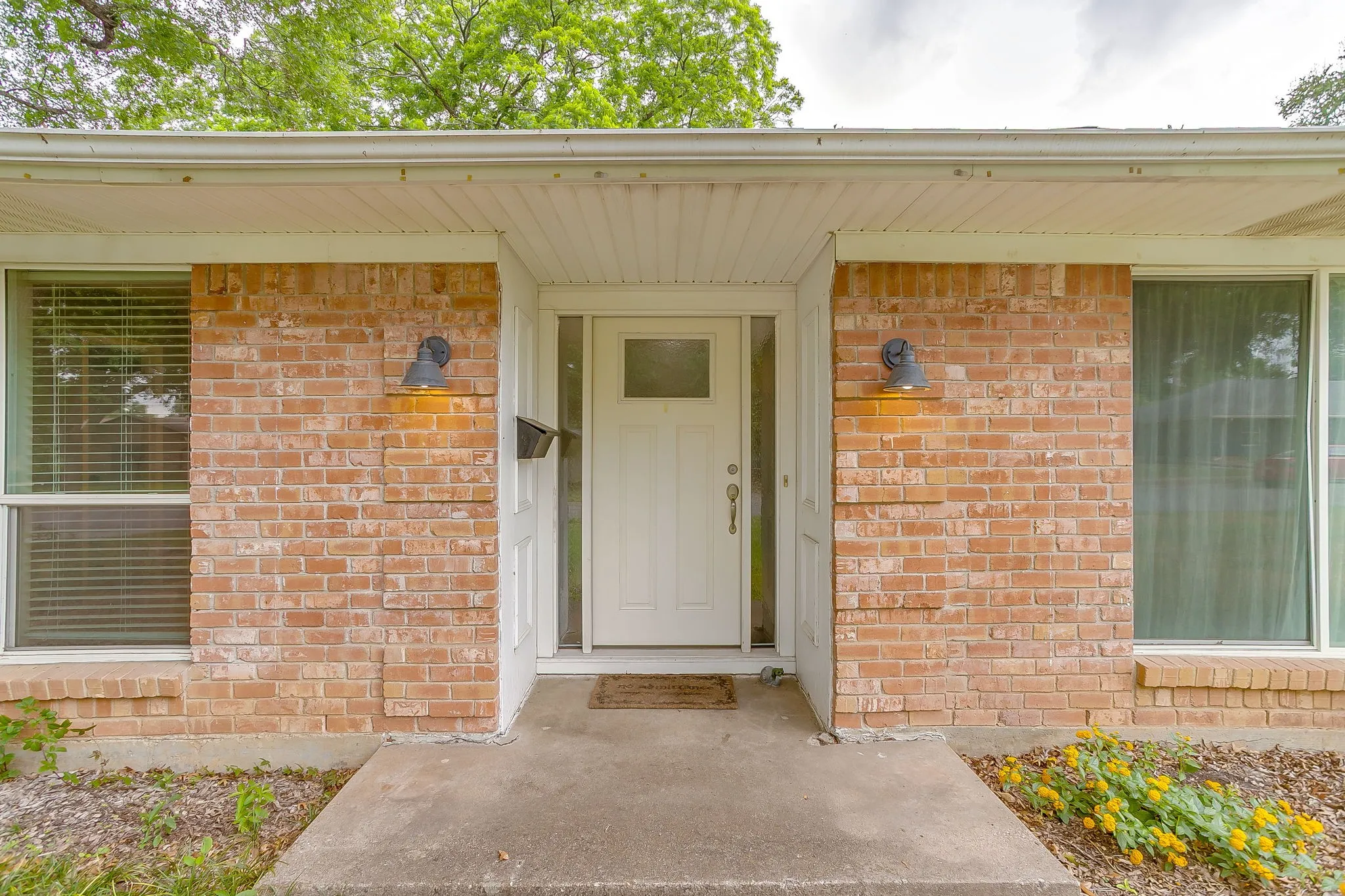 Brick facade entryway with a white front door, transom window, and dual exterior wall sconces