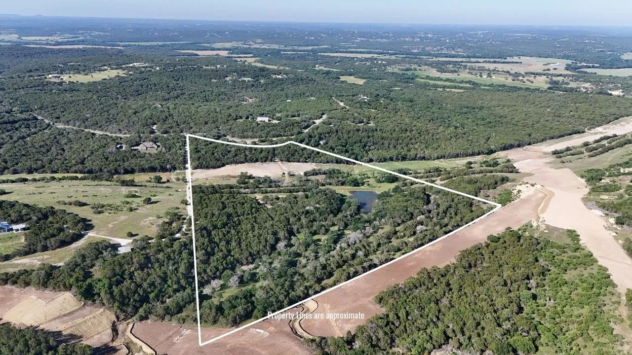 Expansive land parcel featuring dense tree coverage, open fields, and a visible pond