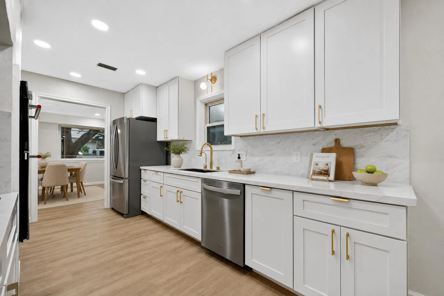 Modern kitchen featuring white shaker cabinetry with gold-tone hardware, stainless steel appliances, white countertops, and a white marble-look backsplash
