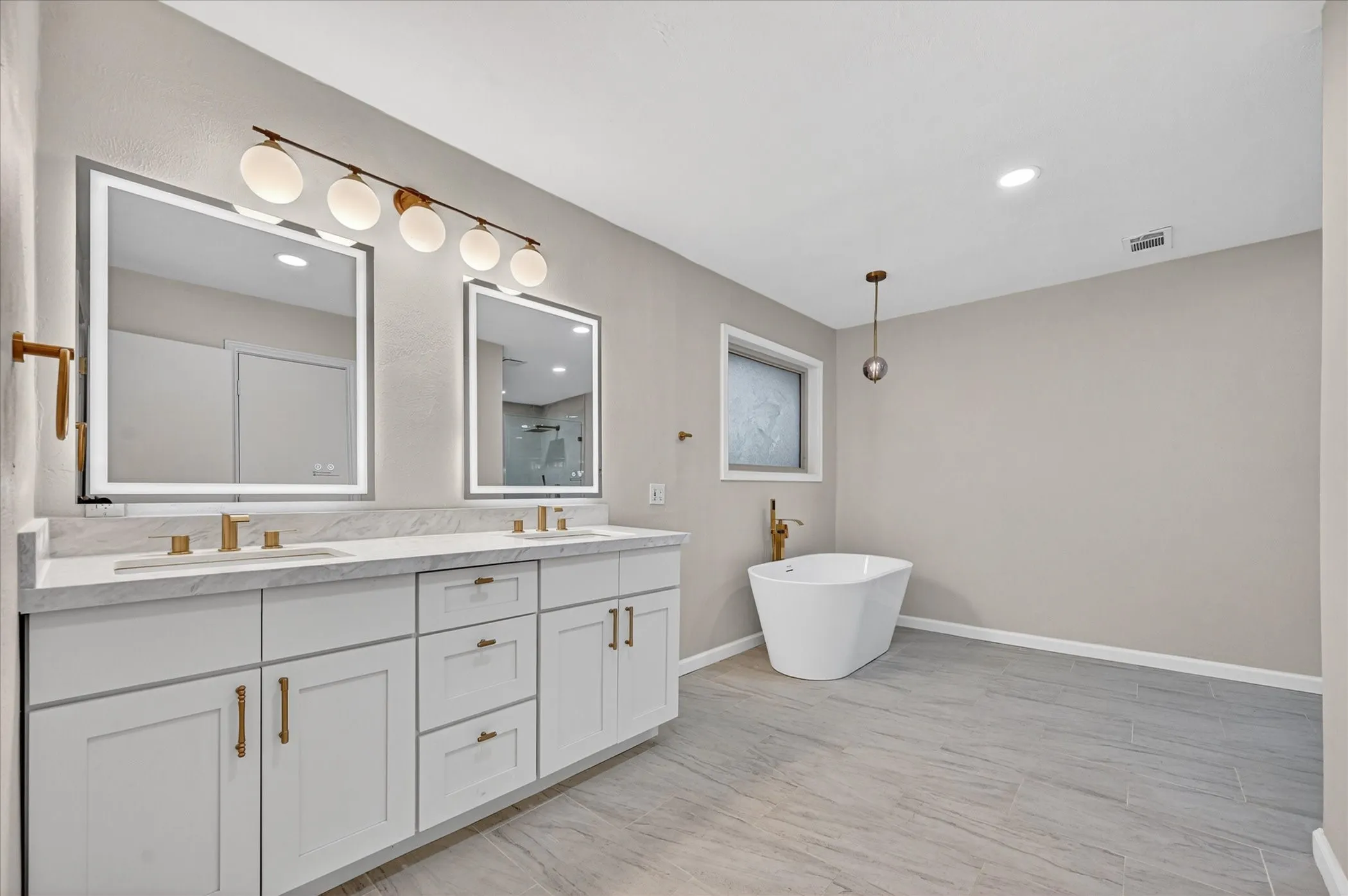 Dual vanity with white cabinetry, gold-tone hardware, and integrated lighting
