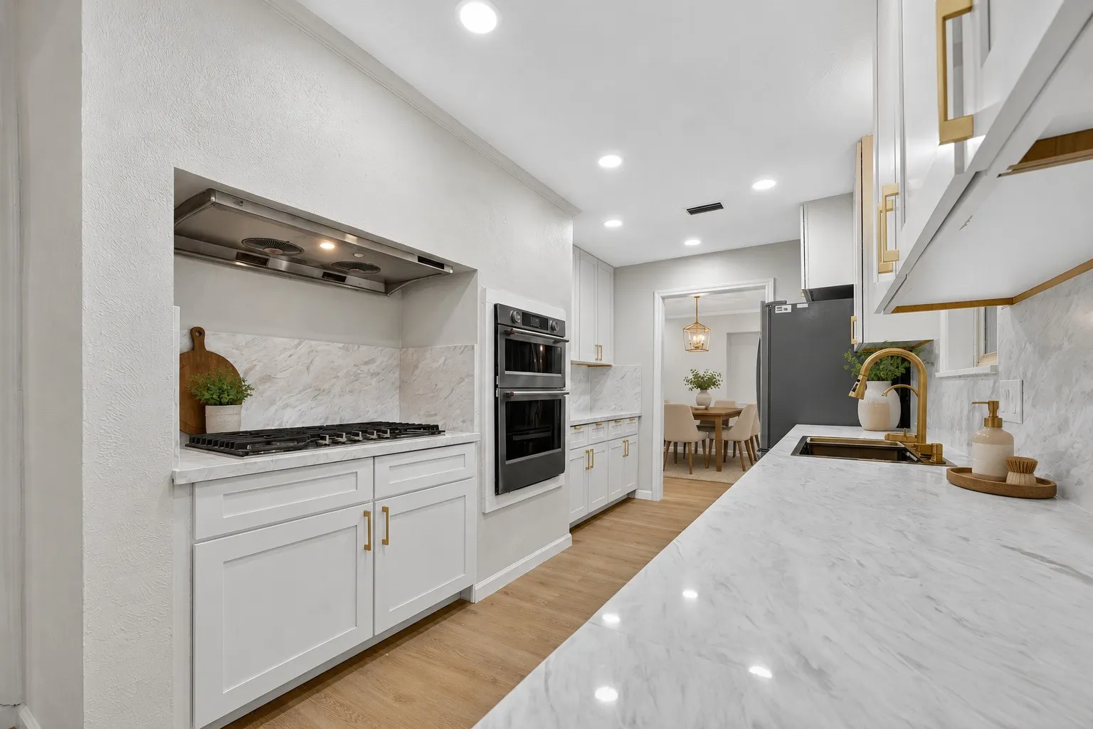 Gourmet kitchen featuring a gas range with built-in hood, double wall ovens, marble countertops, and light wood-finish flooring