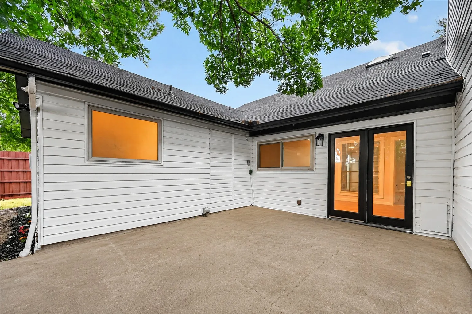 Spacious patio featuring a concrete surface, white horizontal siding, and black-framed French doors