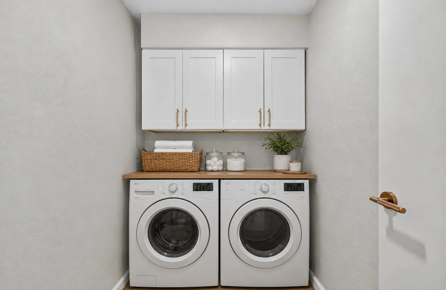 Dedicated laundry area featuring white shaker-style cabinetry with gold-tone hardware, a wood-finish countertop, and light gray wall finishes