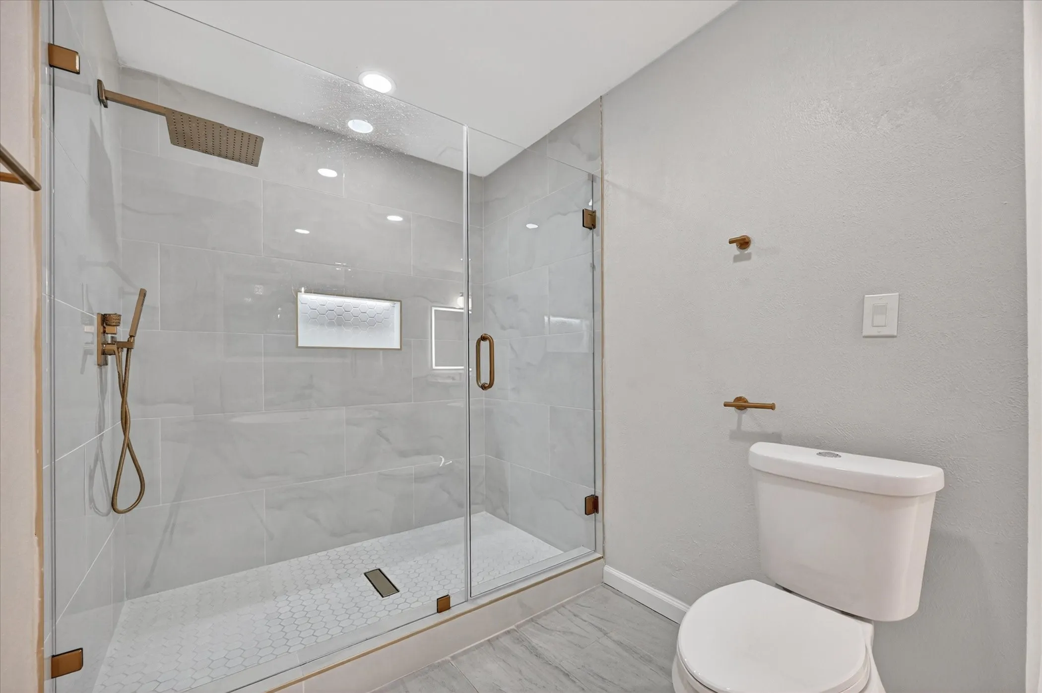Frameless glass shower enclosure featuring a rainfall showerhead and handheld sprayer