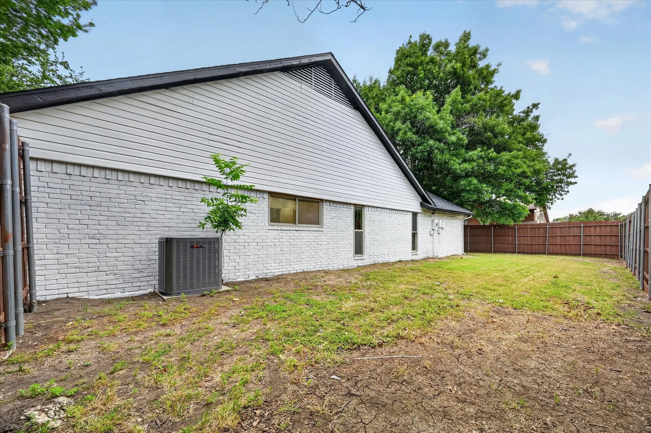 Expansive side yard featuring a partial brick exterior with horizontal siding, a private wood fence, and a mature tree