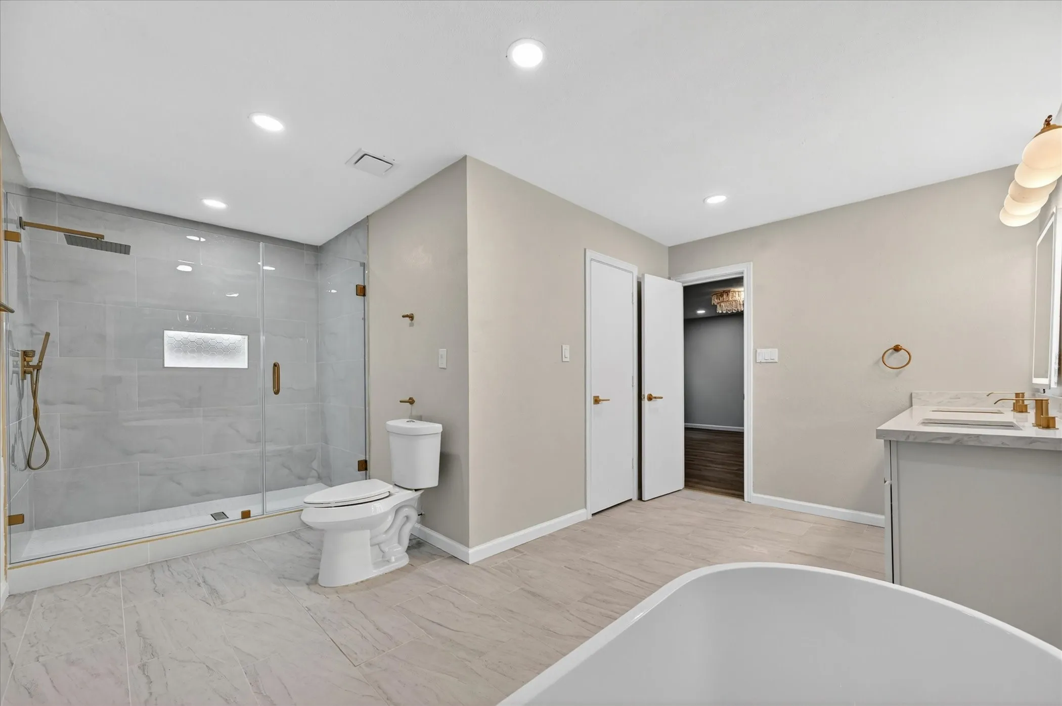 Spacious bathroom featuring a frameless glass shower with gold-tone fixtures, a built-in shower niche, and large format tile flooring