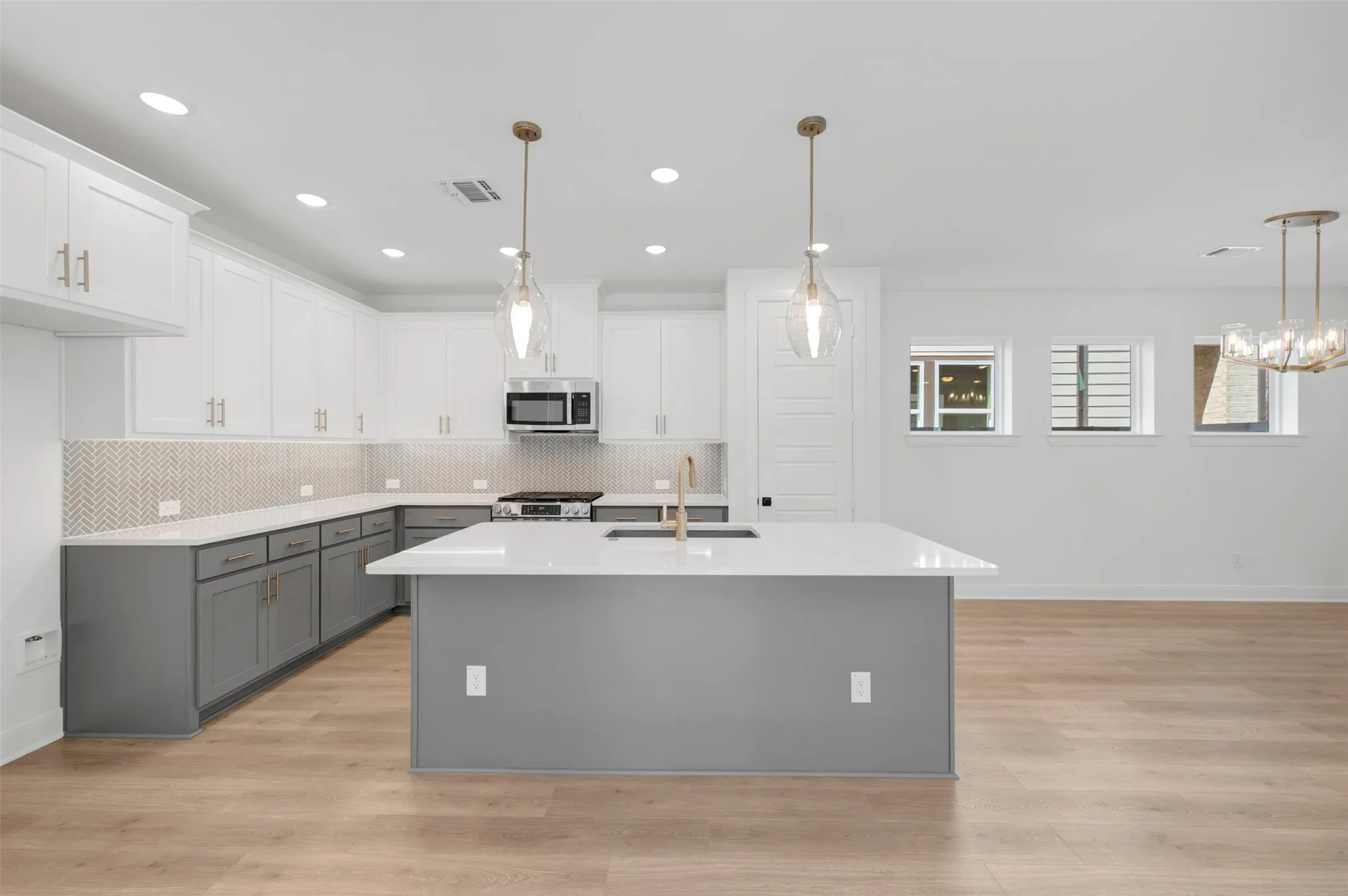 Open-concept kitchen featuring an island with an integrated sink, stainless steel microwave, and herringbone tile backsplash