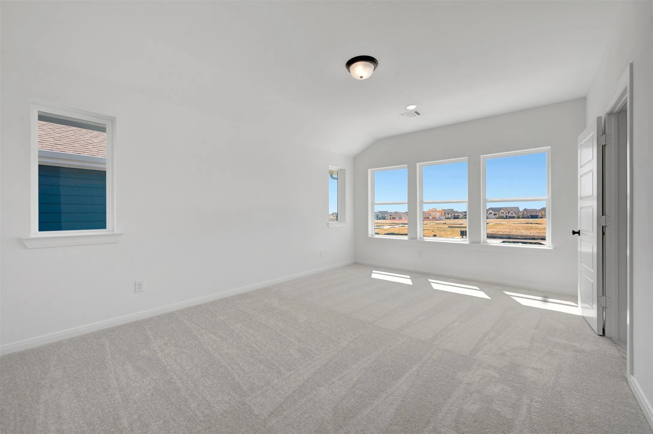Spacious room featuring multiple windows, neutral carpeting, and a semi-flush mount ceiling light