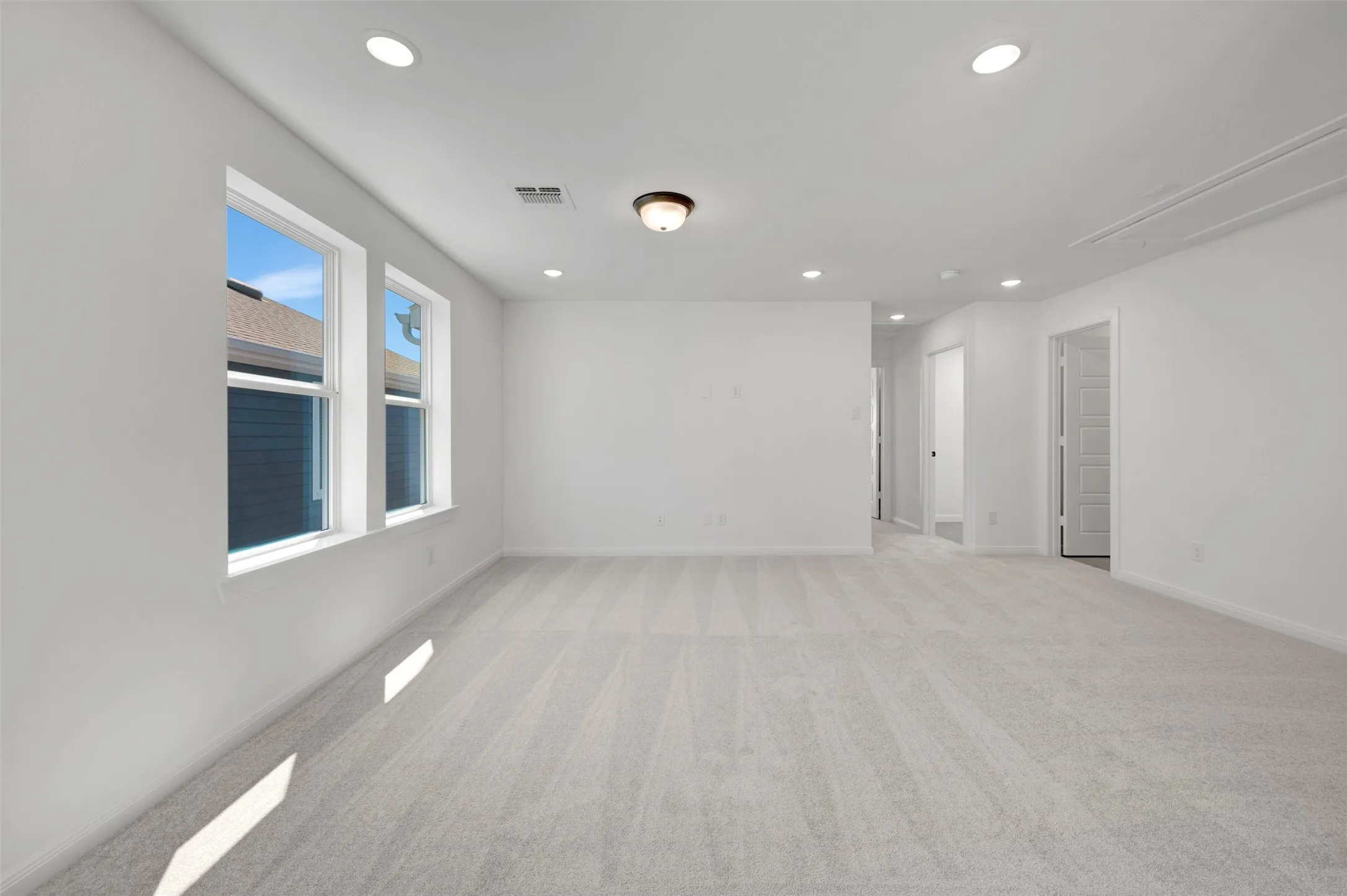 Expansive room featuring light-toned carpeting, multiple recessed lights, a central flush-mount fixture, and two large windows with white trim