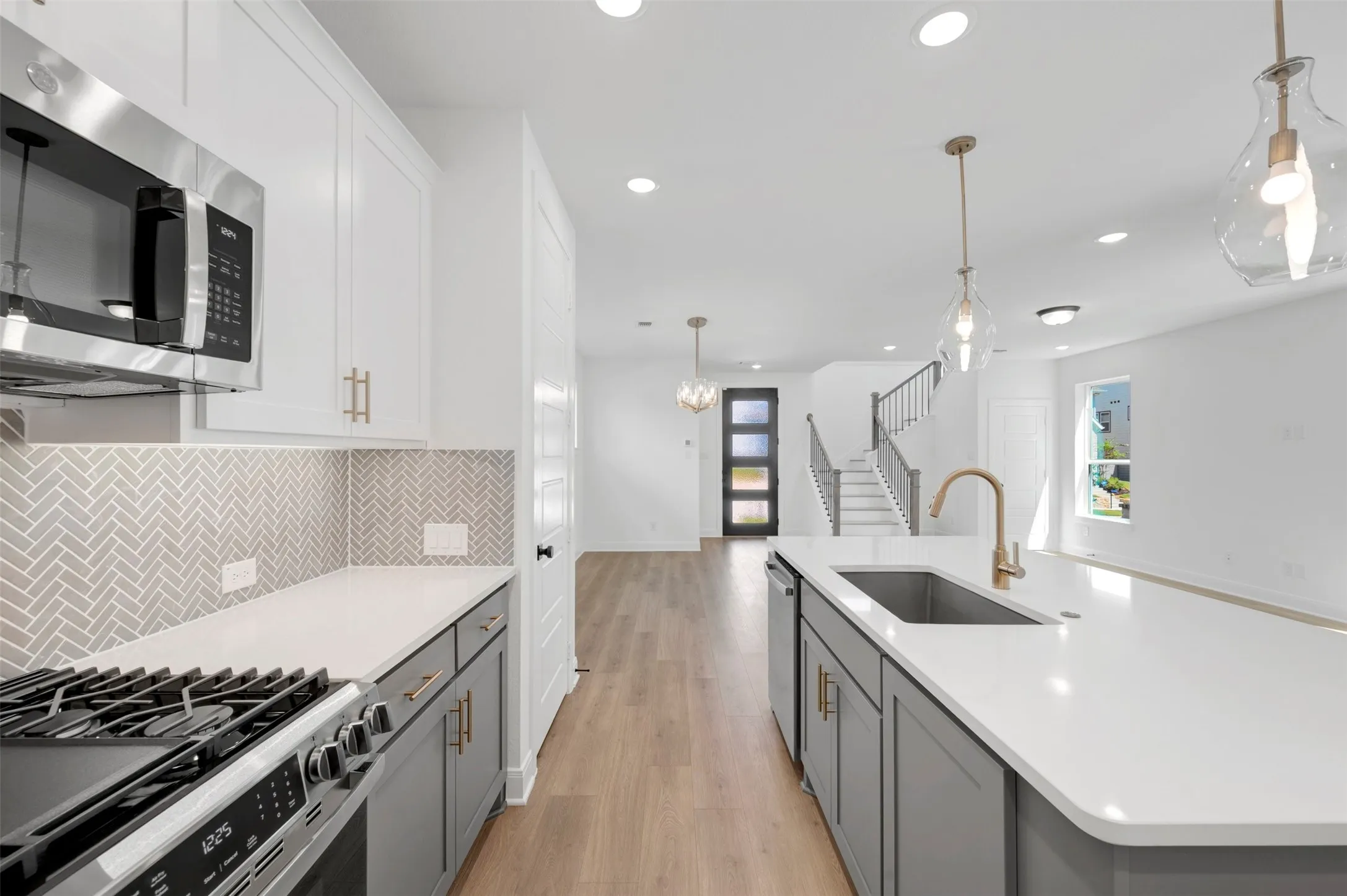 Open-concept kitchen featuring an island with an undermount sink, stainless steel appliances, a herringbone tile backsplash, recessed lighting, and wood-finish flooring
