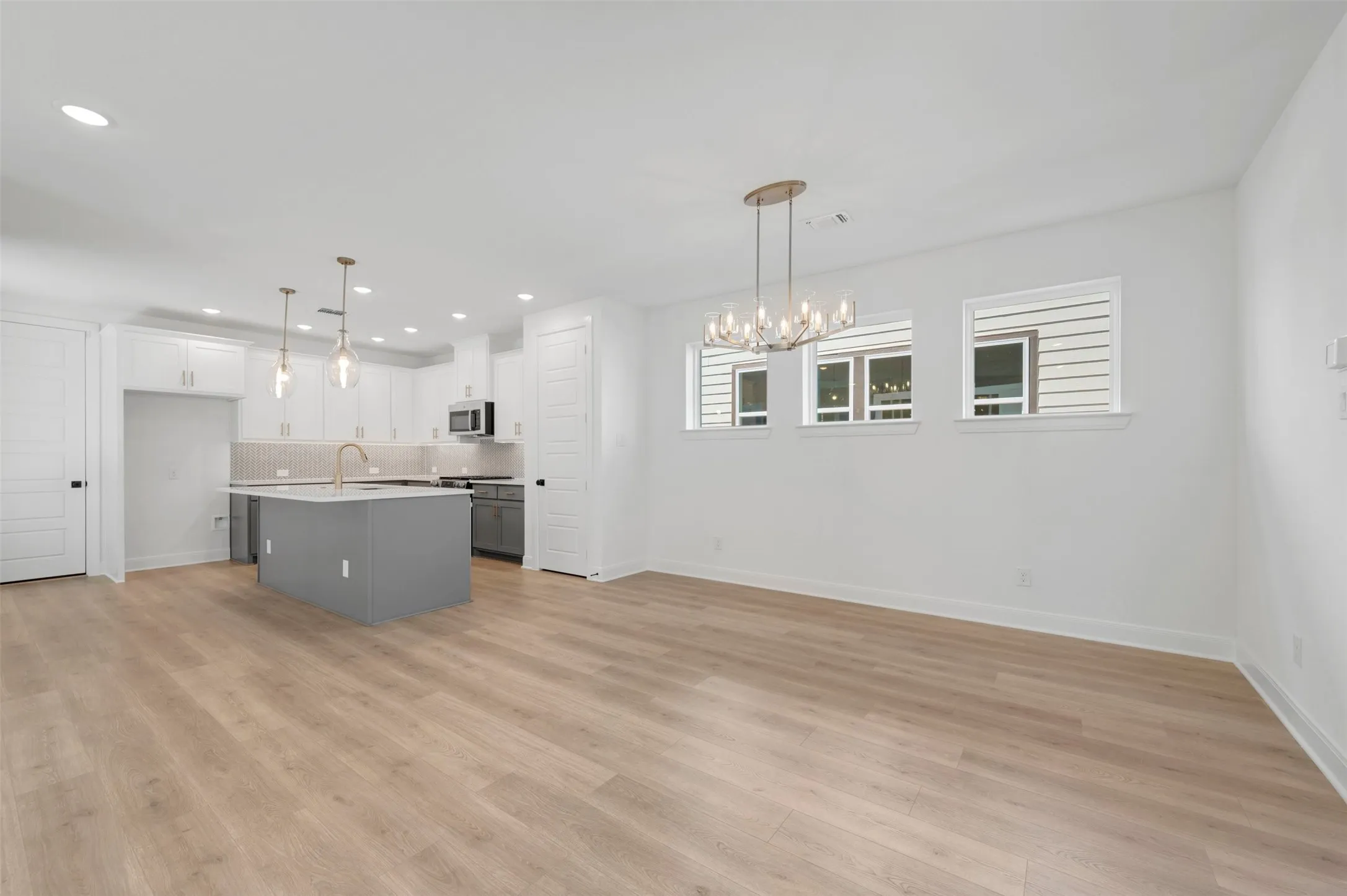 Open-concept living area featuring wood-finish flooring, a modern chandelier, three transom windows, a kitchen island with a basin sink, and pendant lighting