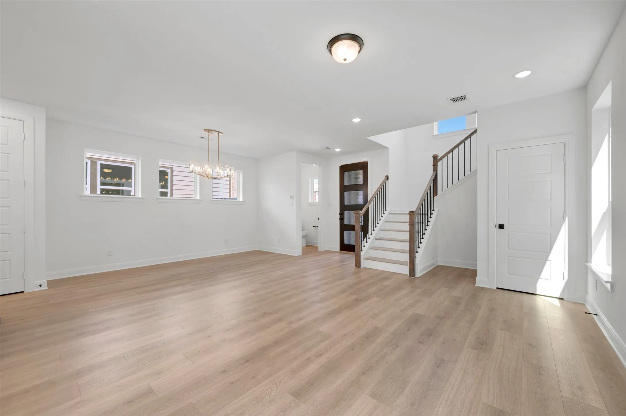 Open-concept living area featuring wood-finish flooring, recessed lighting, and a modern chandelier
