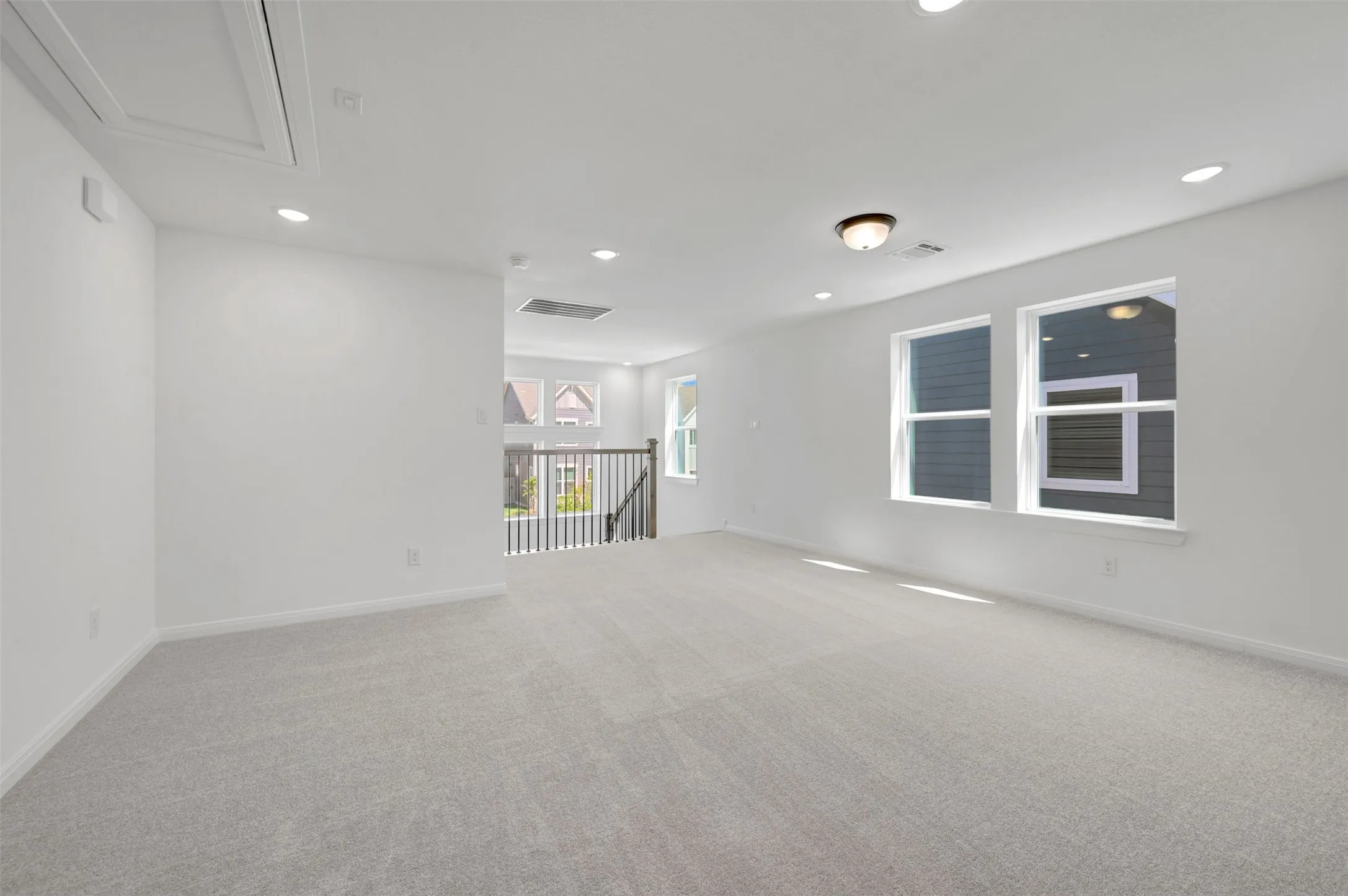Expansive carpeted area with recessed lighting, multiple windows, and a classic spindle railing