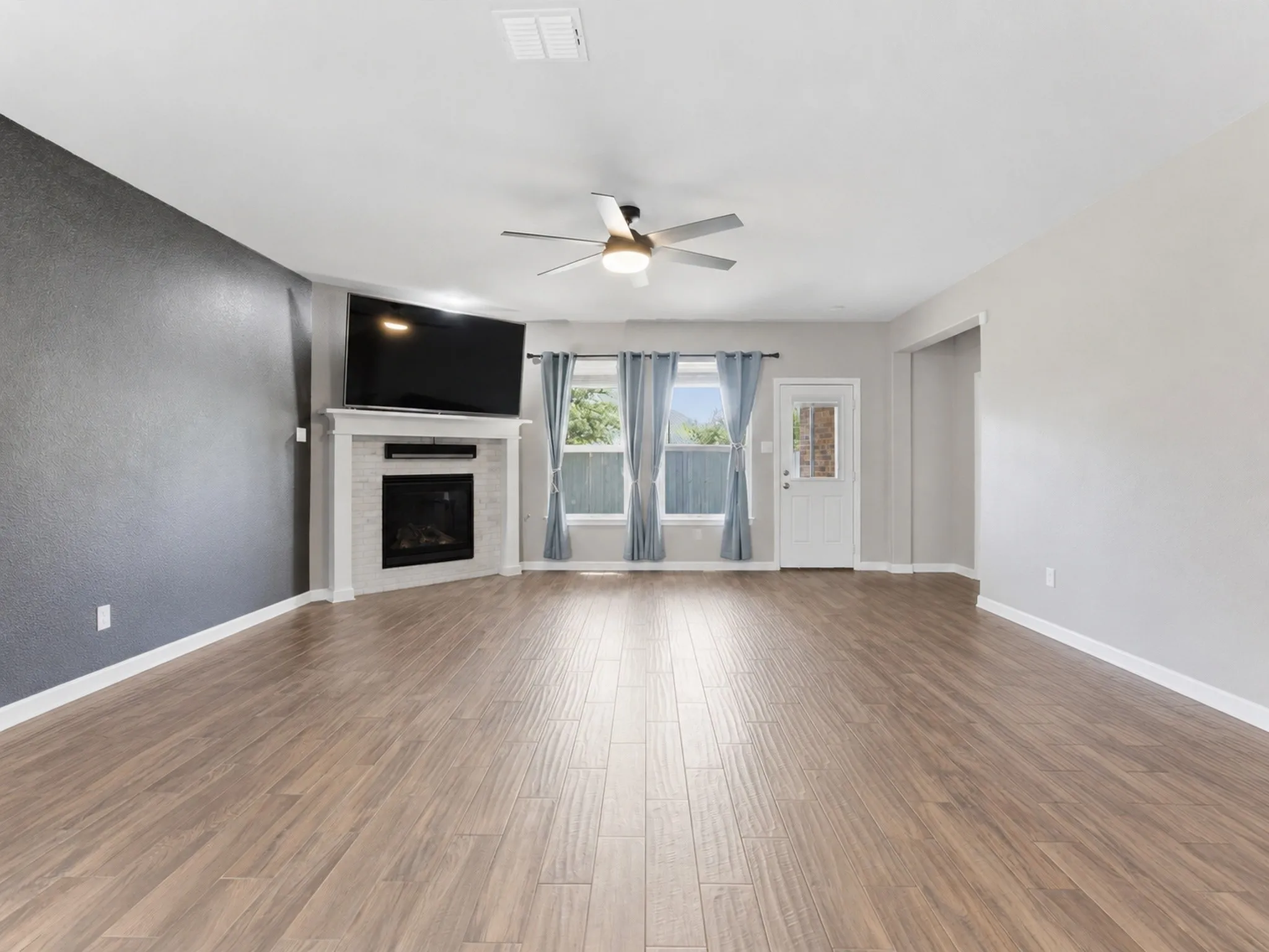 Virtually removed furniture, in Open-concept living space featuring wood-finish flooring, a contemporary ceiling fan, and a fireplace.