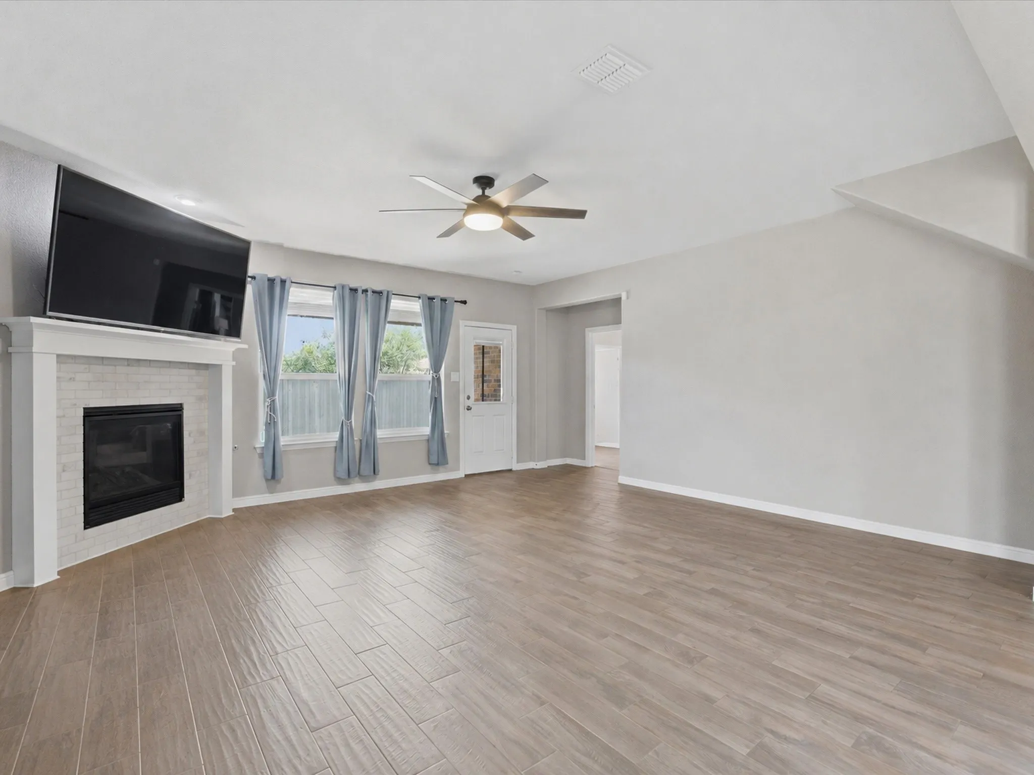 Virtually removed furniture, in Open-concept living space featuring wood-finish flooring, a contemporary ceiling fan, and a fireplace.
