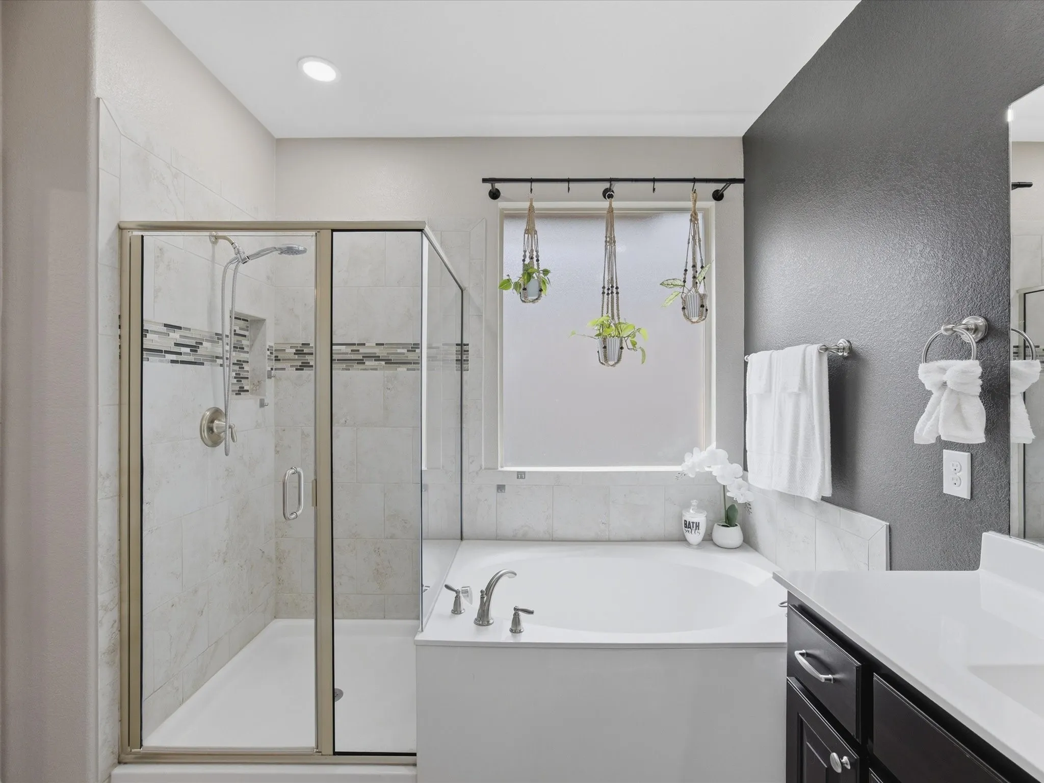 Bathroom featuring a glass-enclosed shower with tile surround, a built-in bathtub with tile decking, a window with privacy blind, and a dark wood vanity with a white countertop and undermount sink