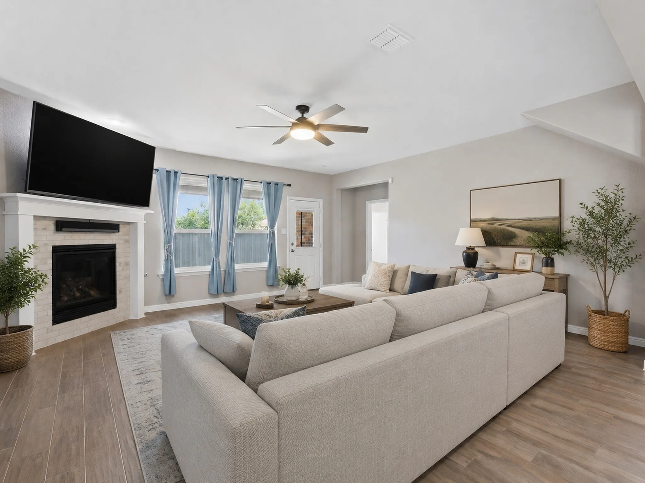 VIRTUALLY STAGED spacious living area featuring light wood-finish flooring, a contemporary fireplace with white tile surround and mantel, and a ceiling fan.