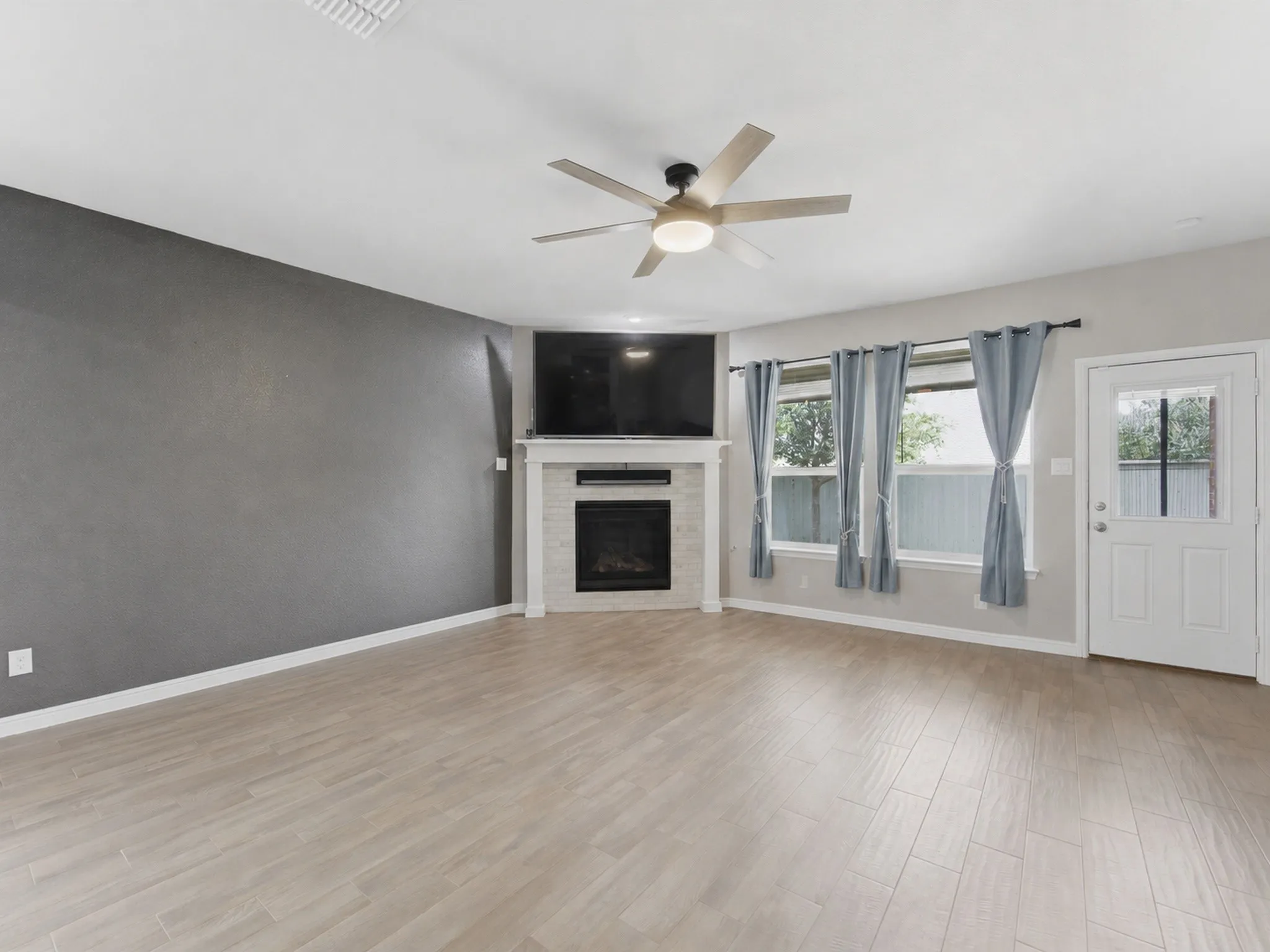 Virtually removed furniture, in Open-concept living space featuring wood-finish flooring, a contemporary ceiling fan, and a fireplace.